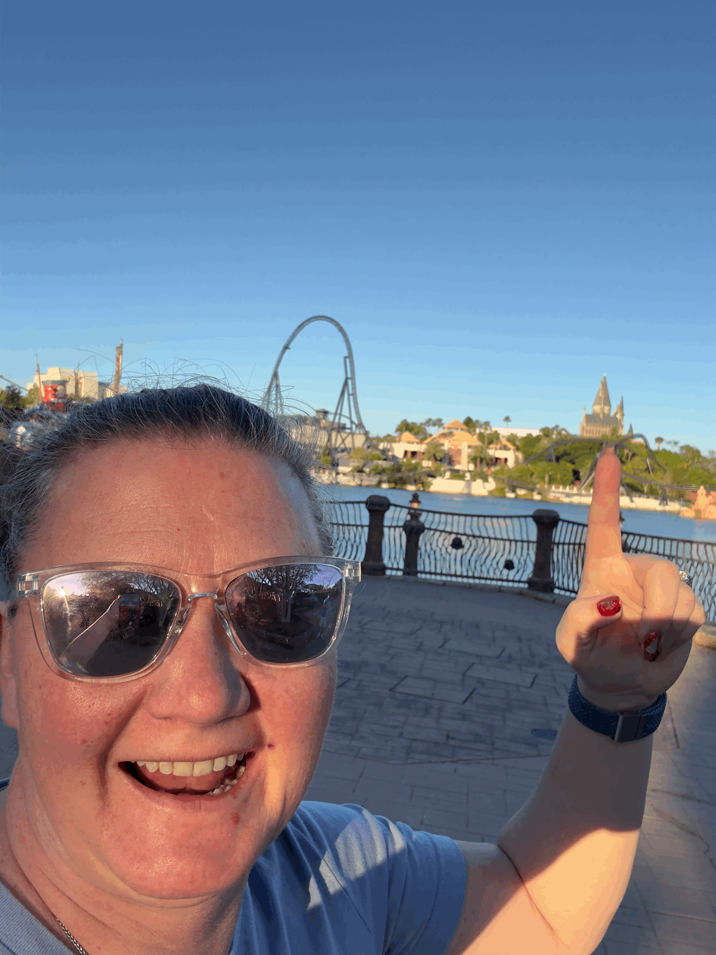 Woman taking selfie at theme park with roller coaster and castle in background