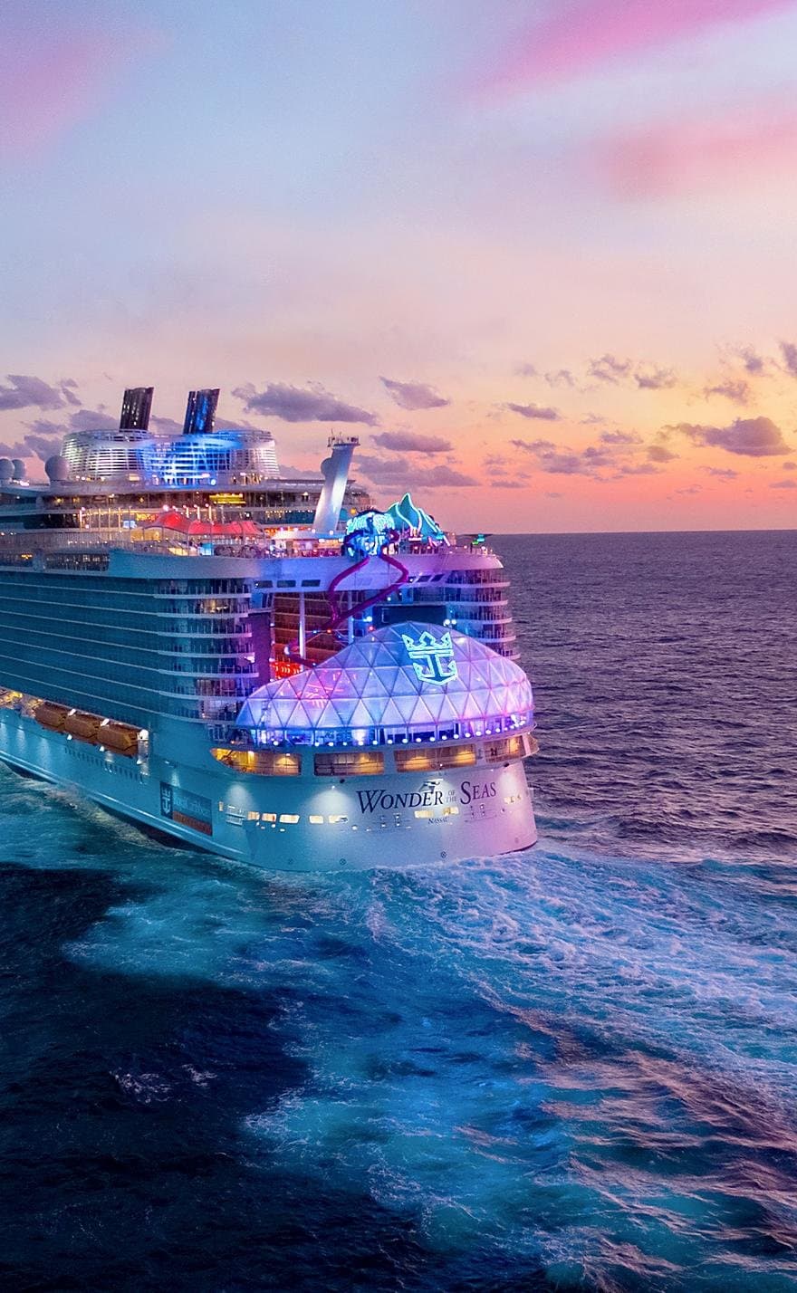 Wonder of the Seas cruise ship illuminated at sunset with colorful lights reflecting off calm ocean waters.