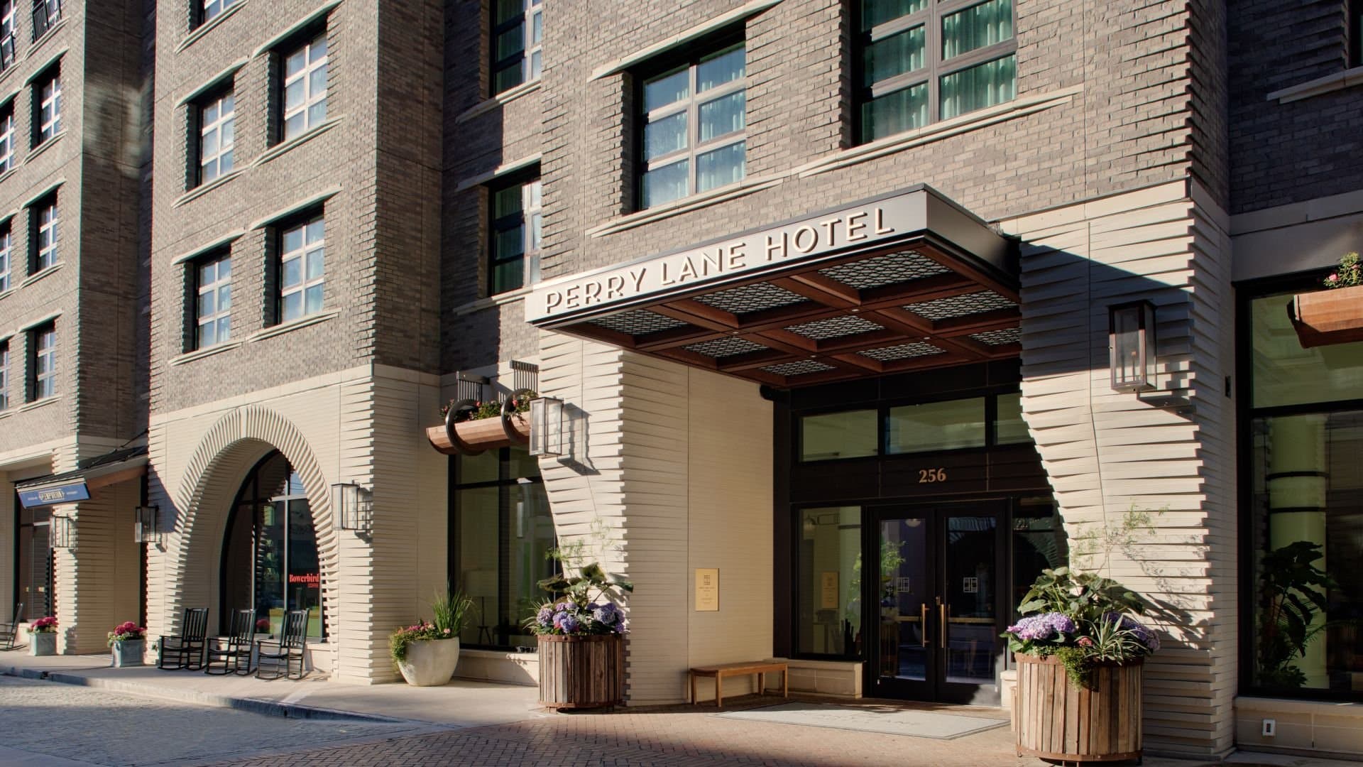 Perry Lane Hotel entrance on a brick street with flowering planters and modern awning in Charleston.