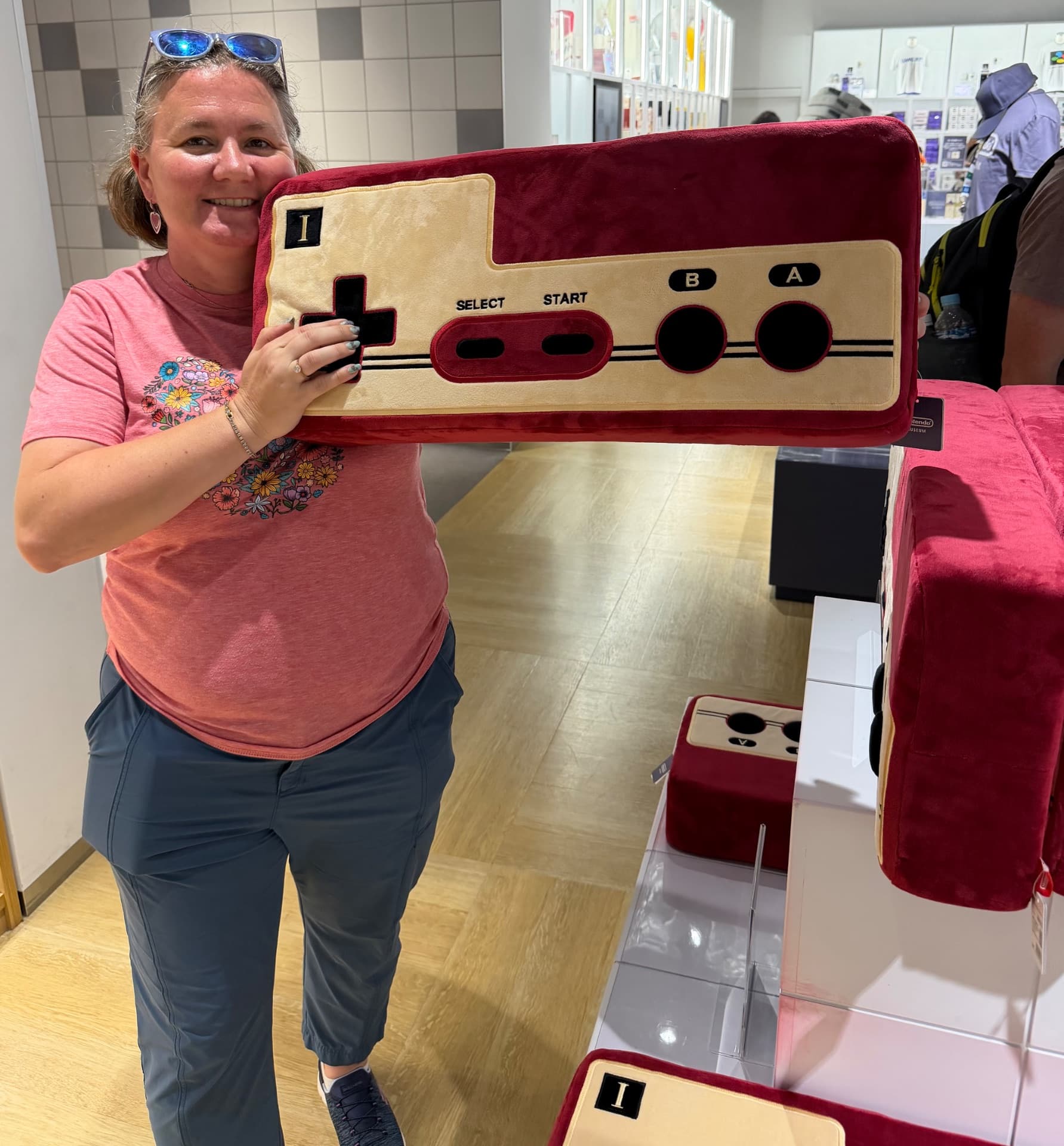 Woman holding a large red and tan NES controller prop in an indoor venue during what appears to be a gaming or pop culture event.