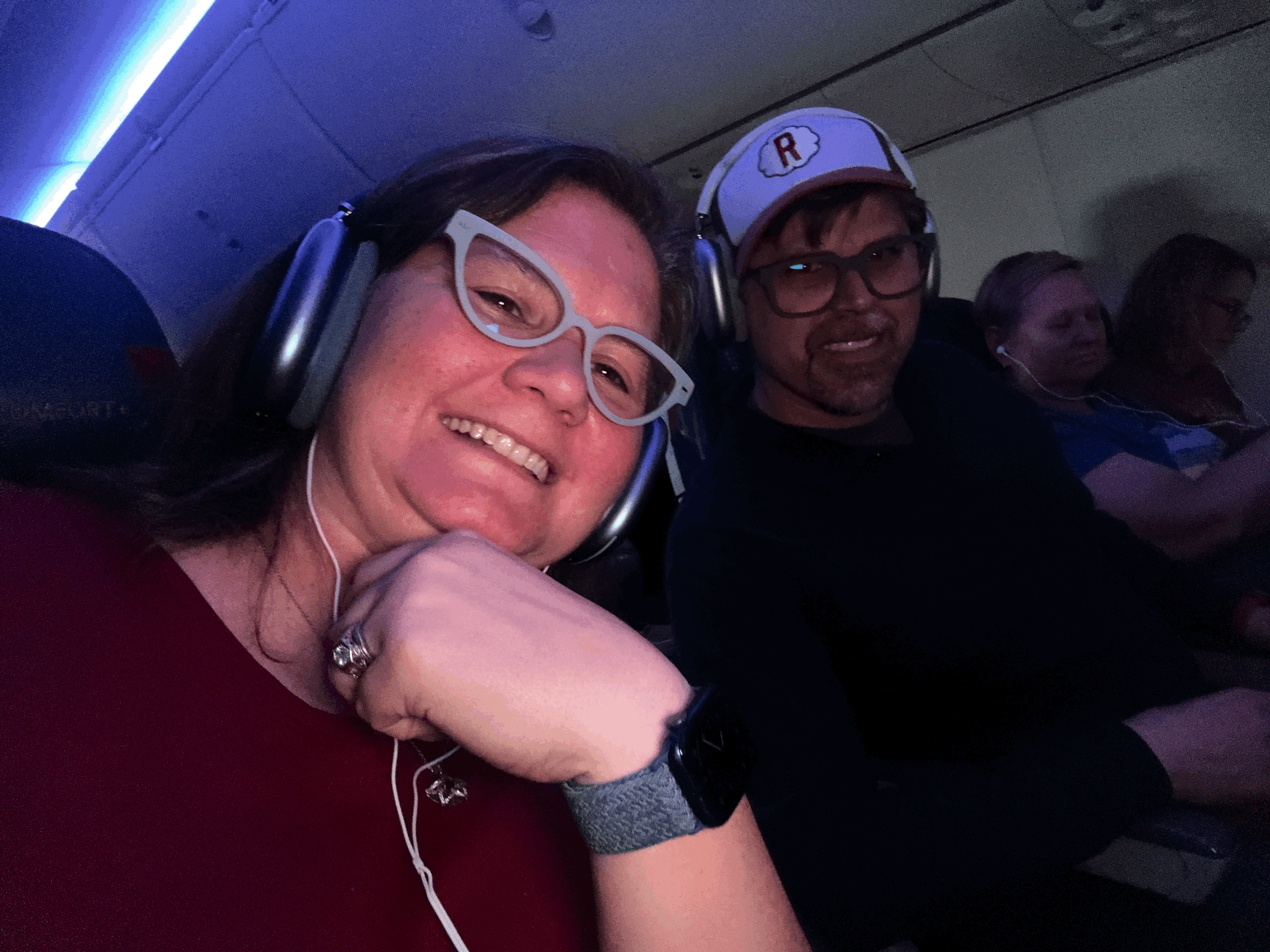 Two people wearing headphones enjoy entertainment on a cruise ship with blue ambient lighting in the background.