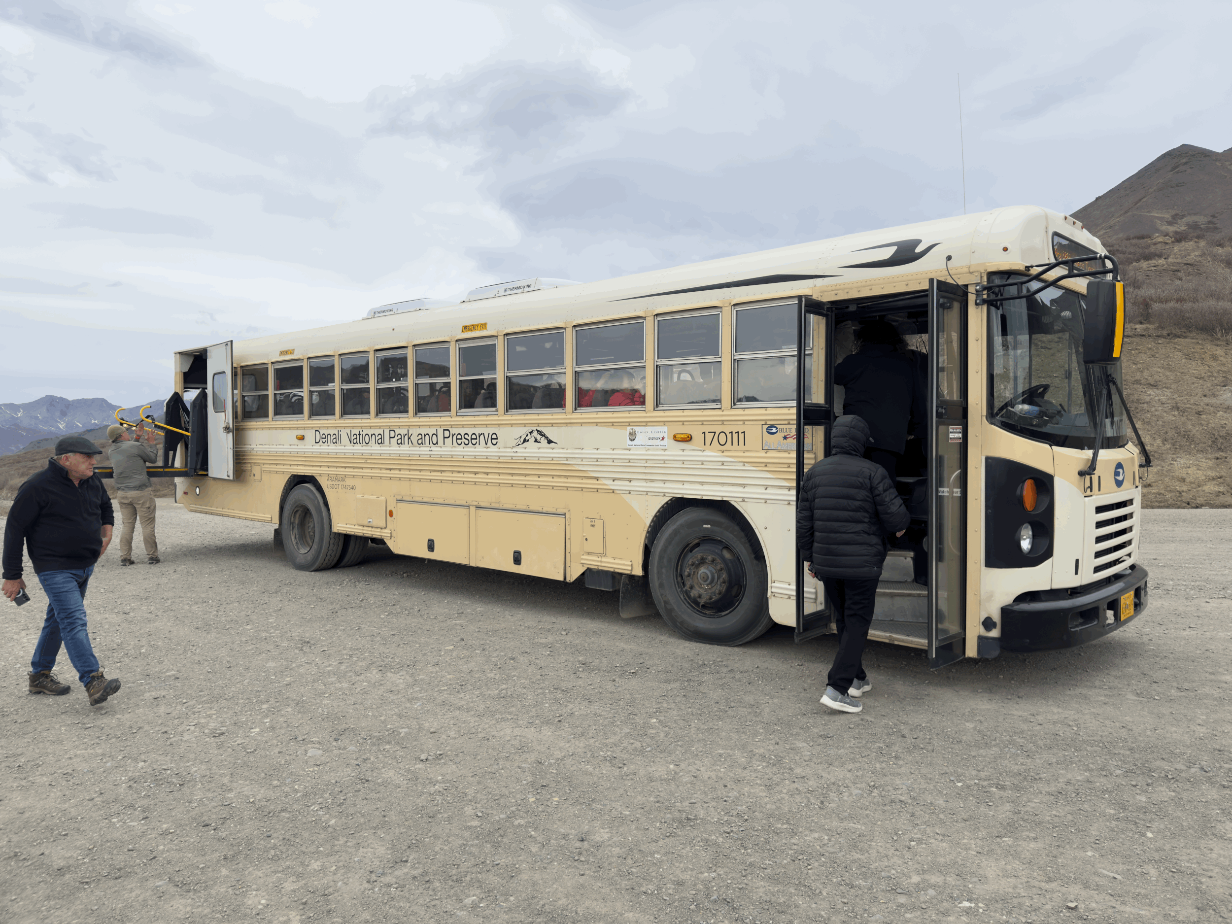 Denali National Park shuttle bus with passengers boarding in Alaska's wilderness landscape.