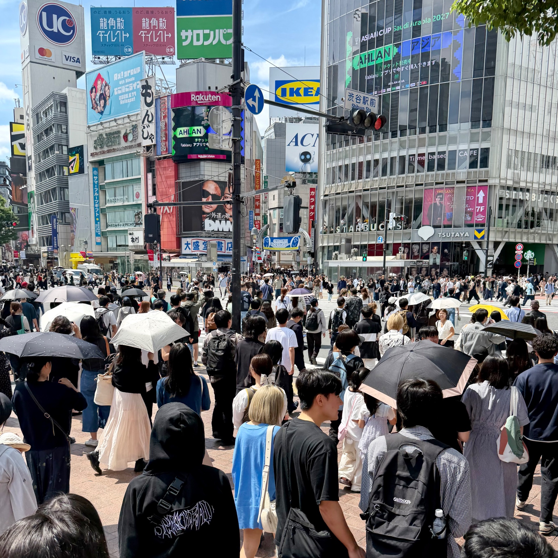 Crowded Shibuya Crossing in Tokyo with hundreds of pedestrians, umbrellas, and colorful commercial signage on surrounding buildings.