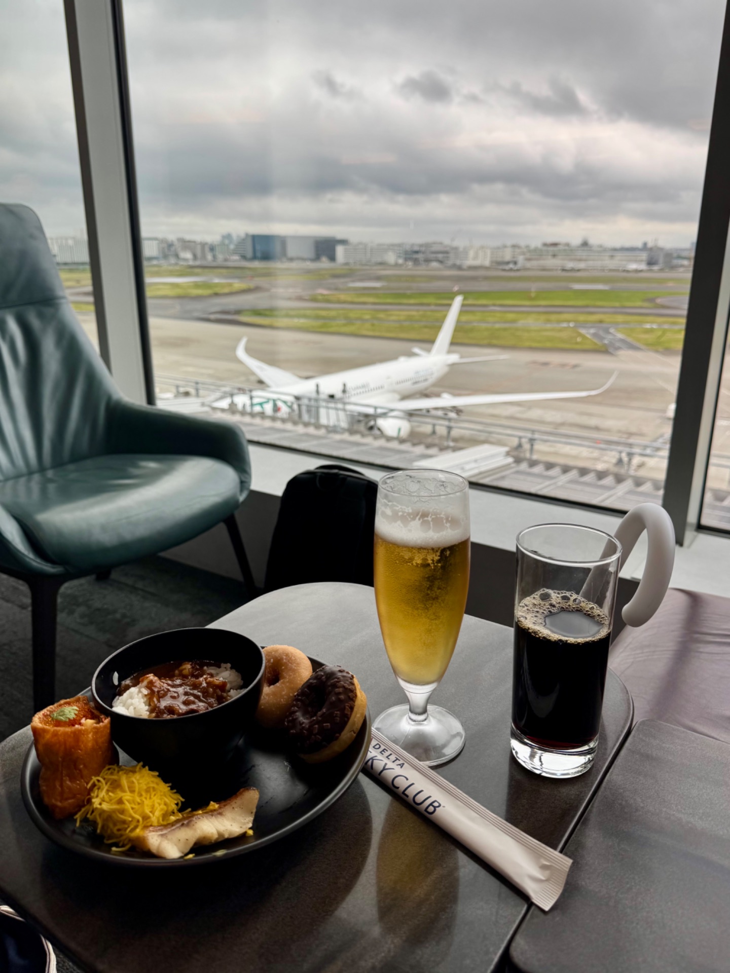 Airport lounge view with food and drinks overlooking parked aircraft and runway tarmac.