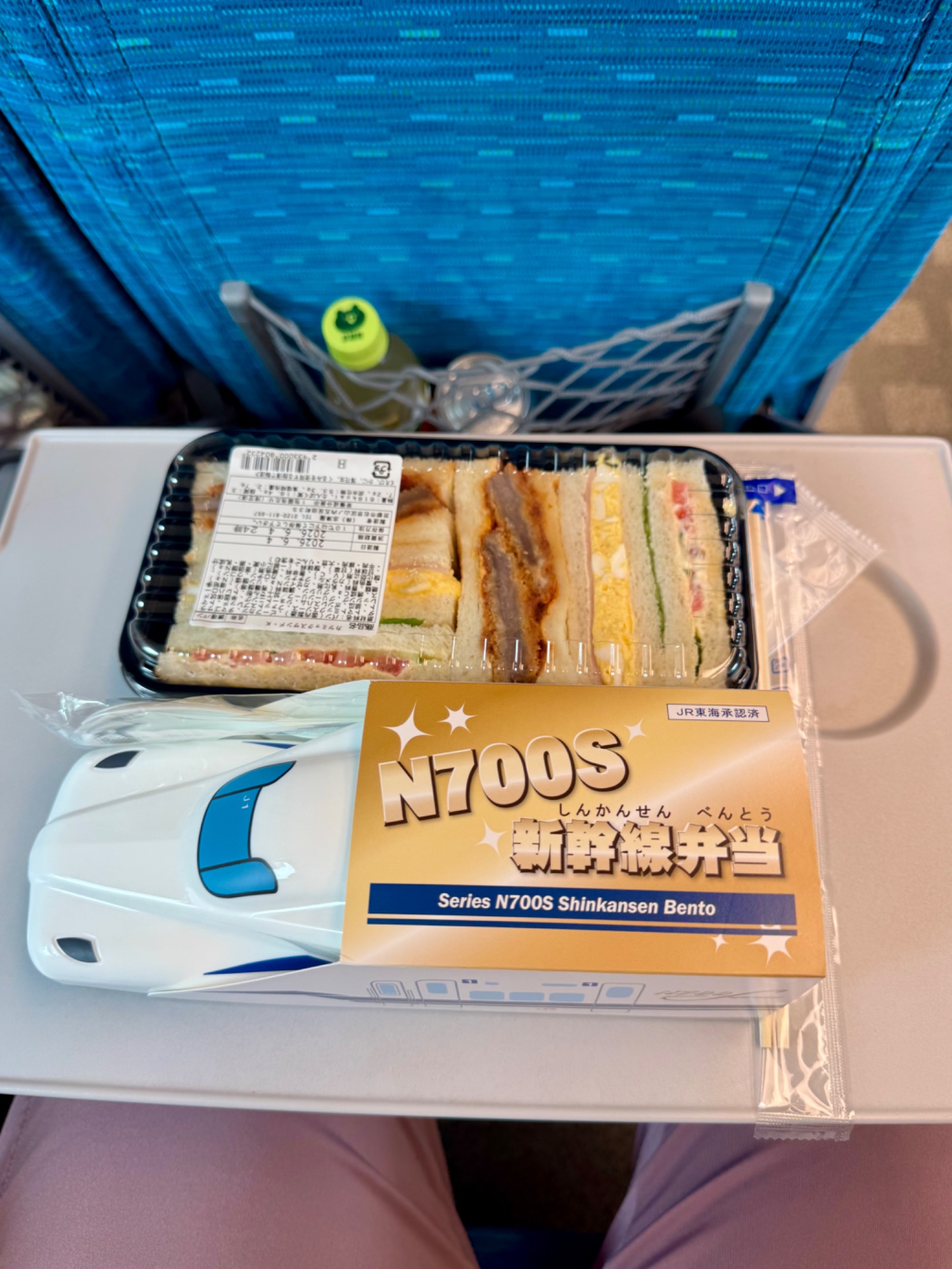 Series N700S Shinkansen bento box with assorted sandwiches and a model train car on display.