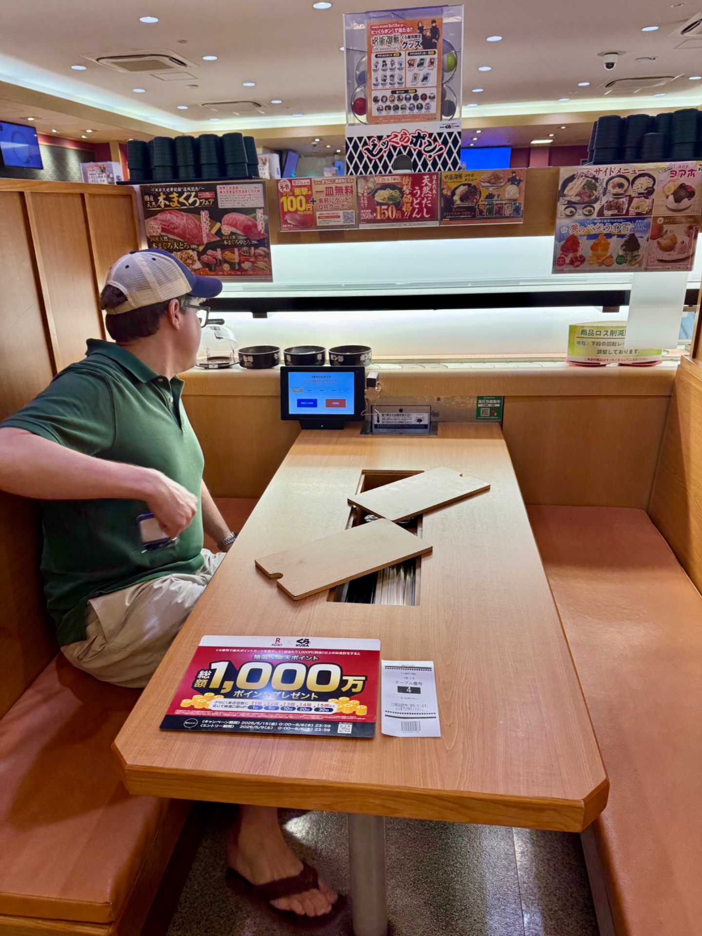 Customer seated at dining table in Japanese restaurant with ordering tablet and promotional signage visible.