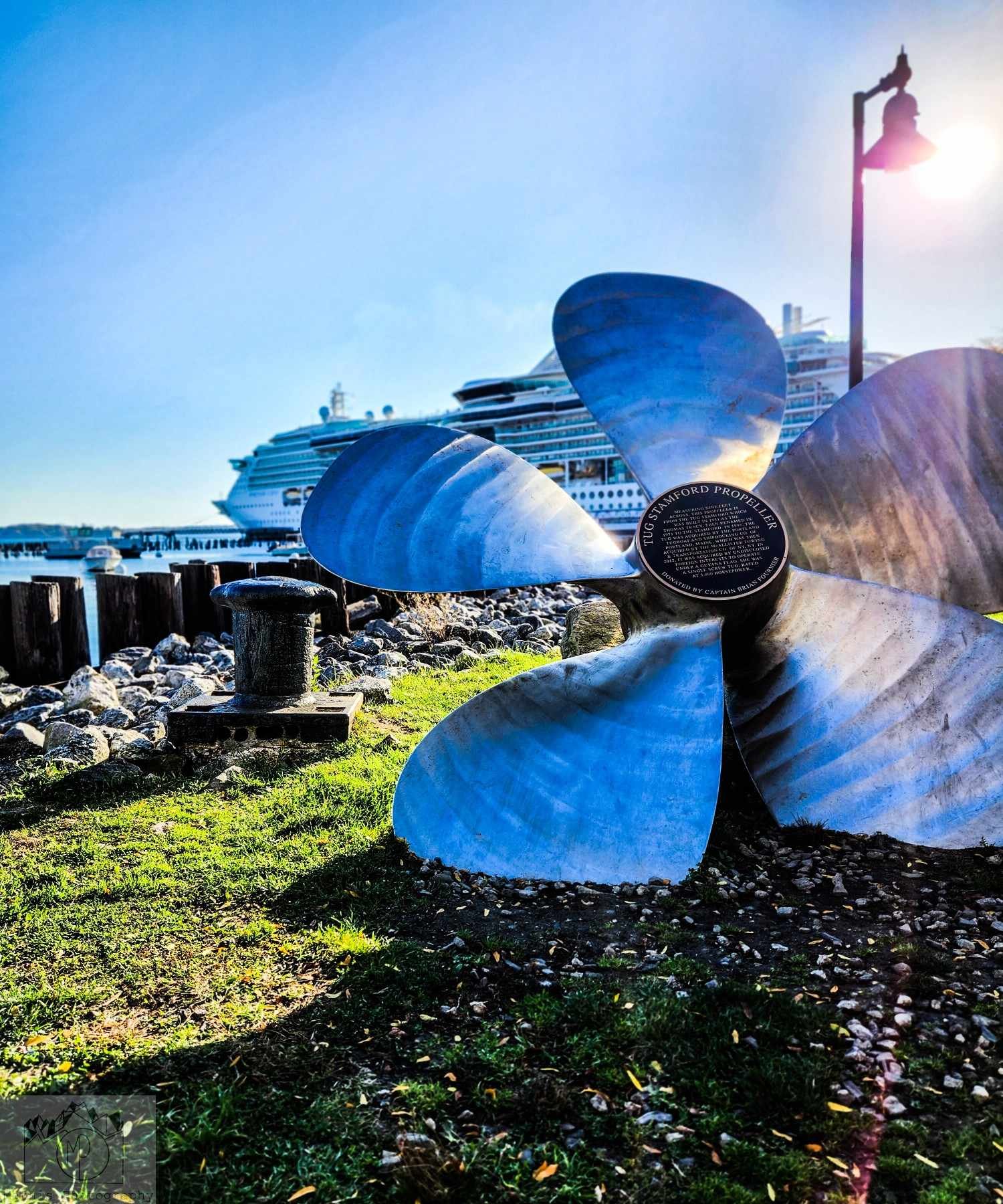 Large blue ship propellers displayed at waterfront with cruise ship
