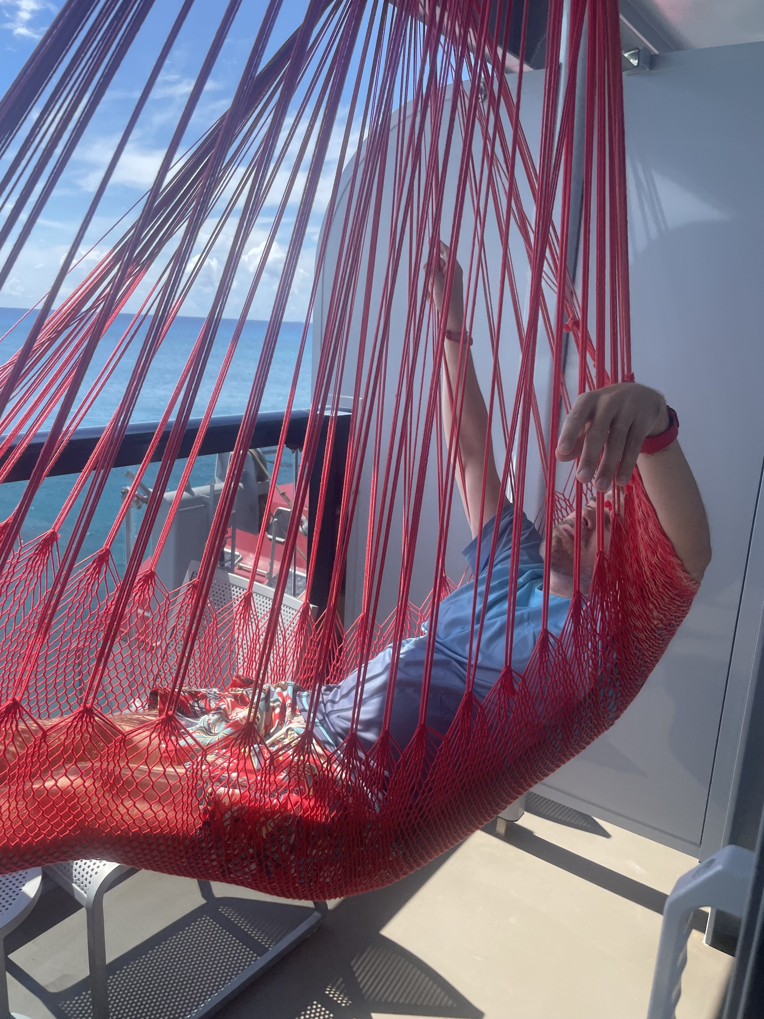 Person relaxing in red hammock on cruise ship deck overlooking ocean