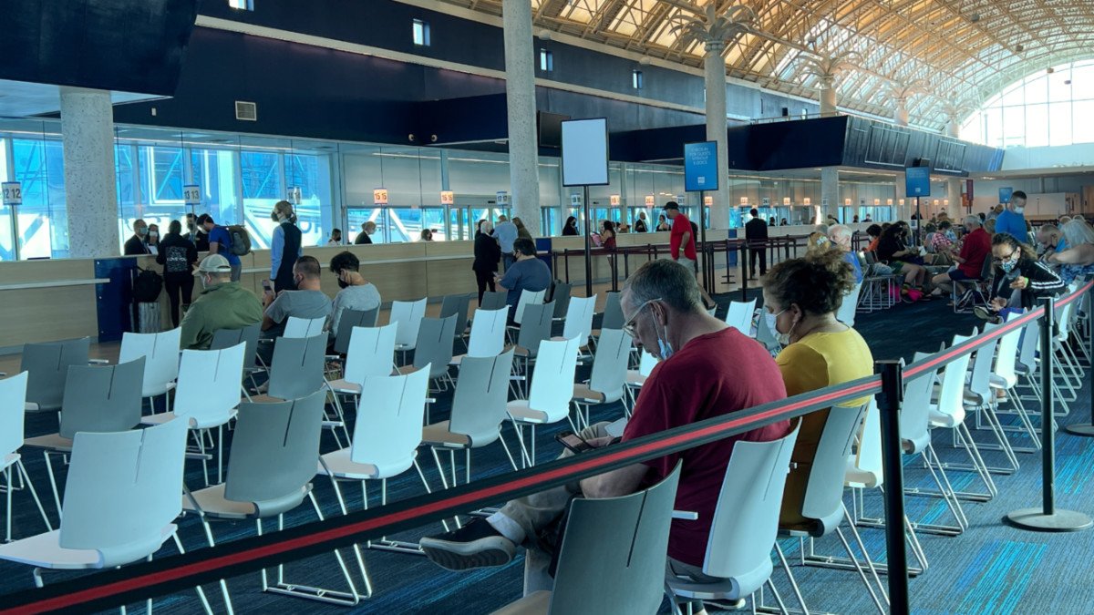 Airport terminal waiting area with passengers seated in white chairs