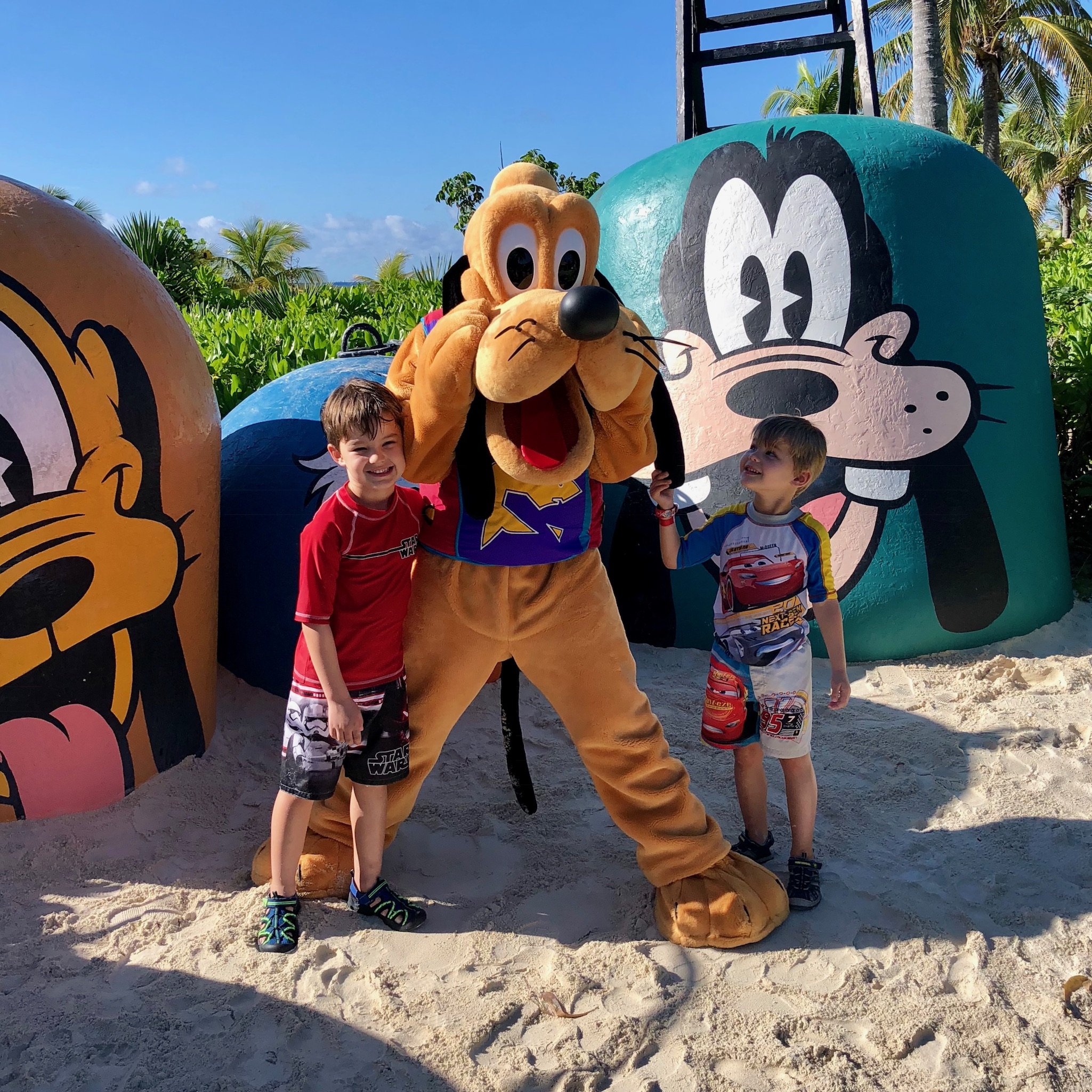 Two boys meet Pluto character on sandy beach deck