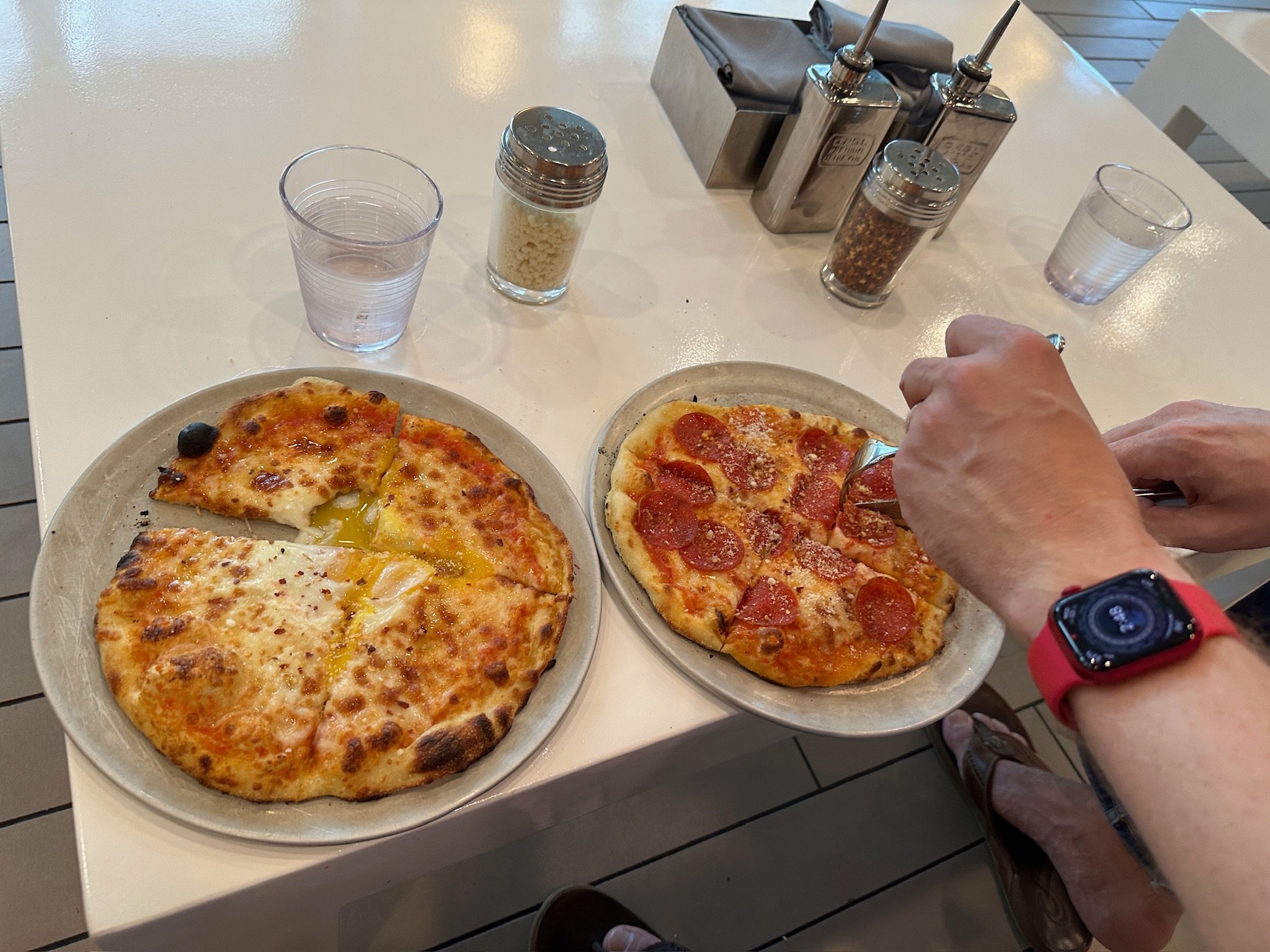 Two pizzas on white table with condiments and water glasses