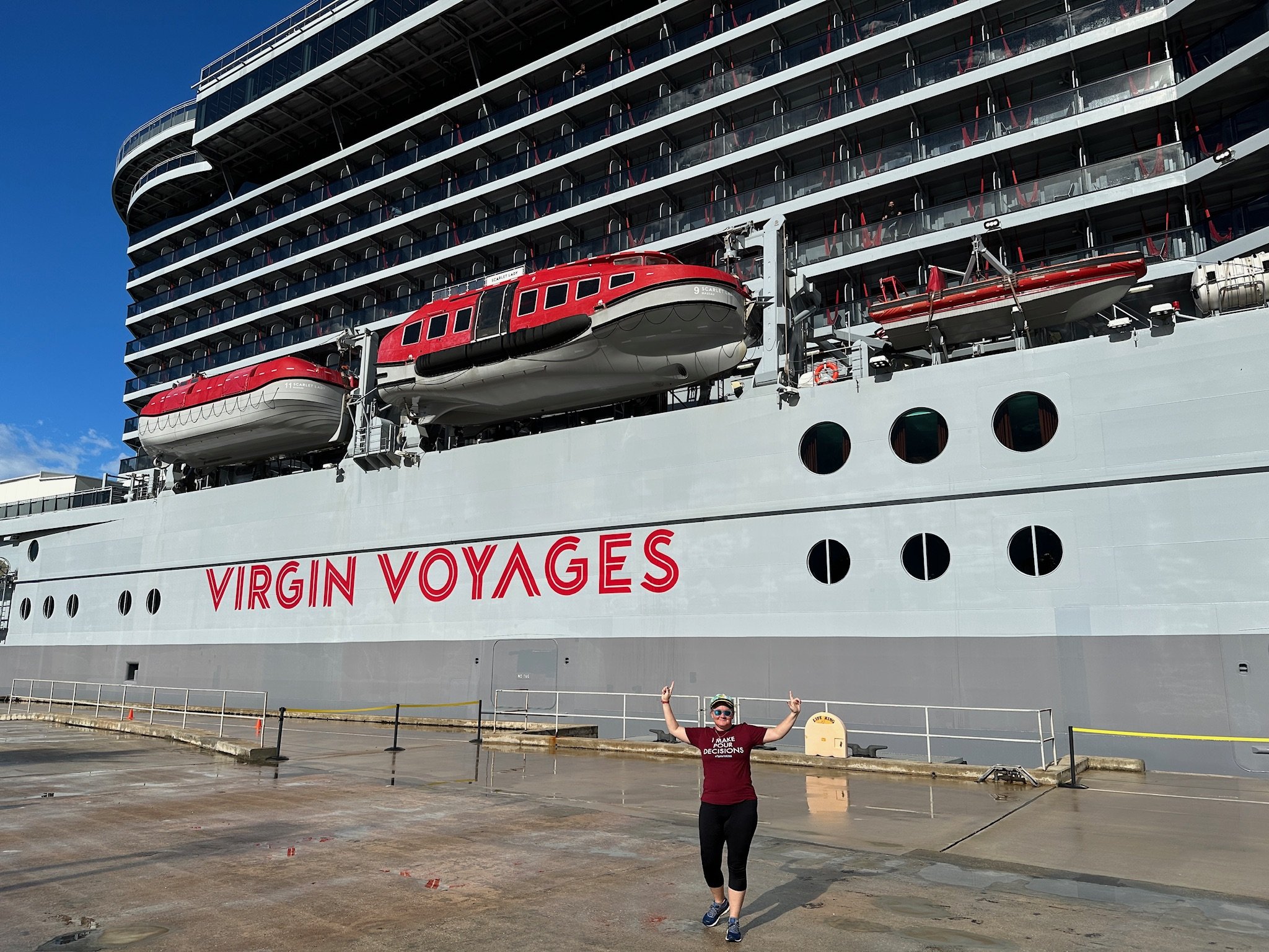 Person posing before Virgin Voyages cruise ship with red tenders
