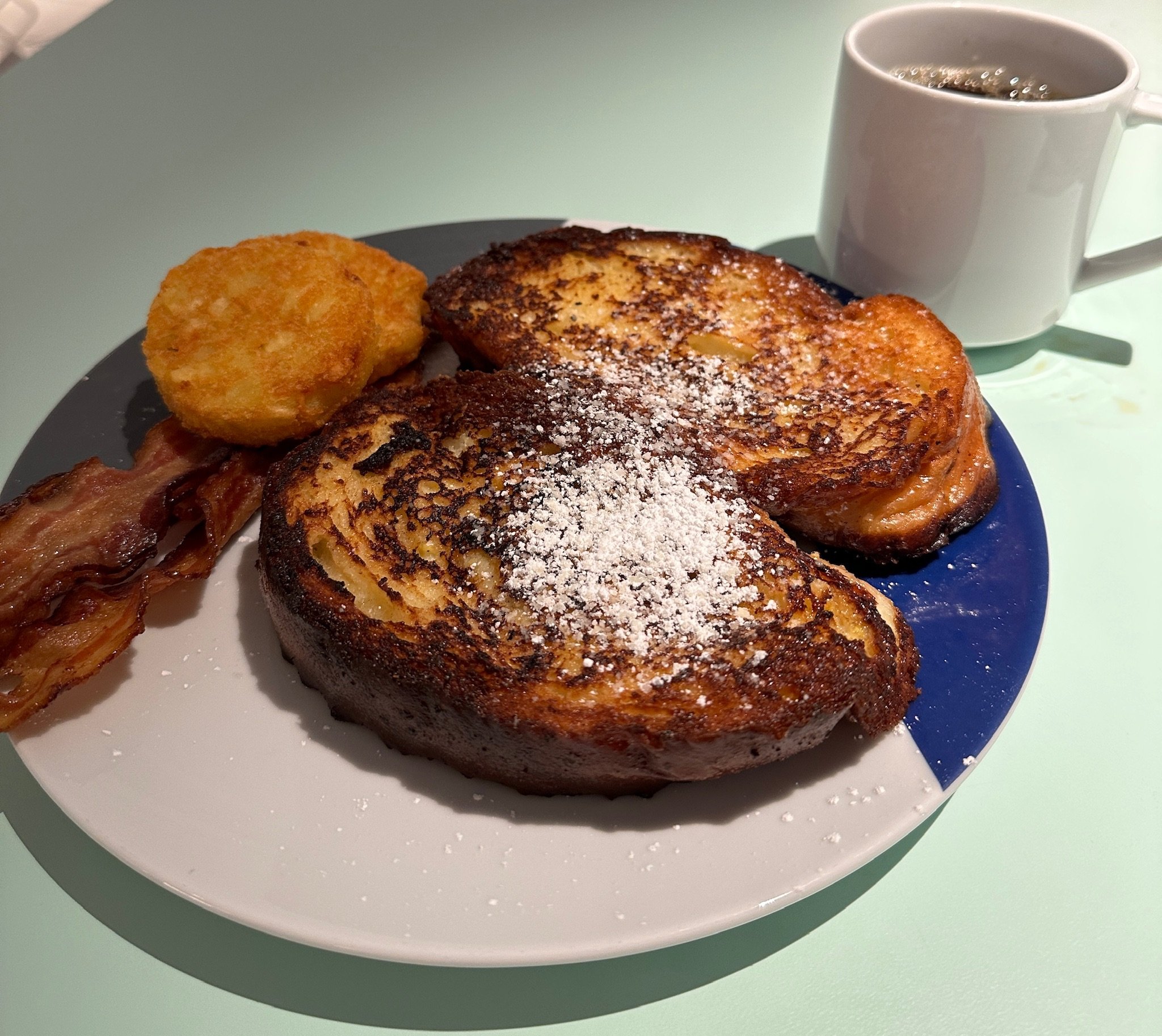 Golden French toast with powdered sugar, bacon, and hash brown