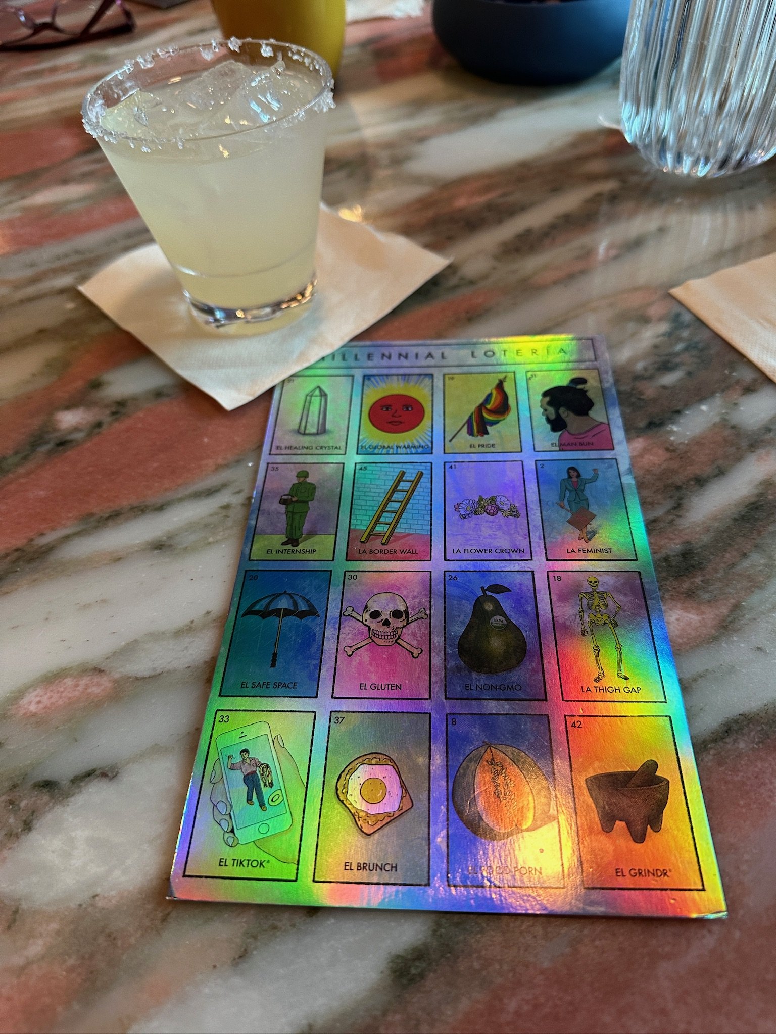 Millennial Loteria card game with margarita on marble table