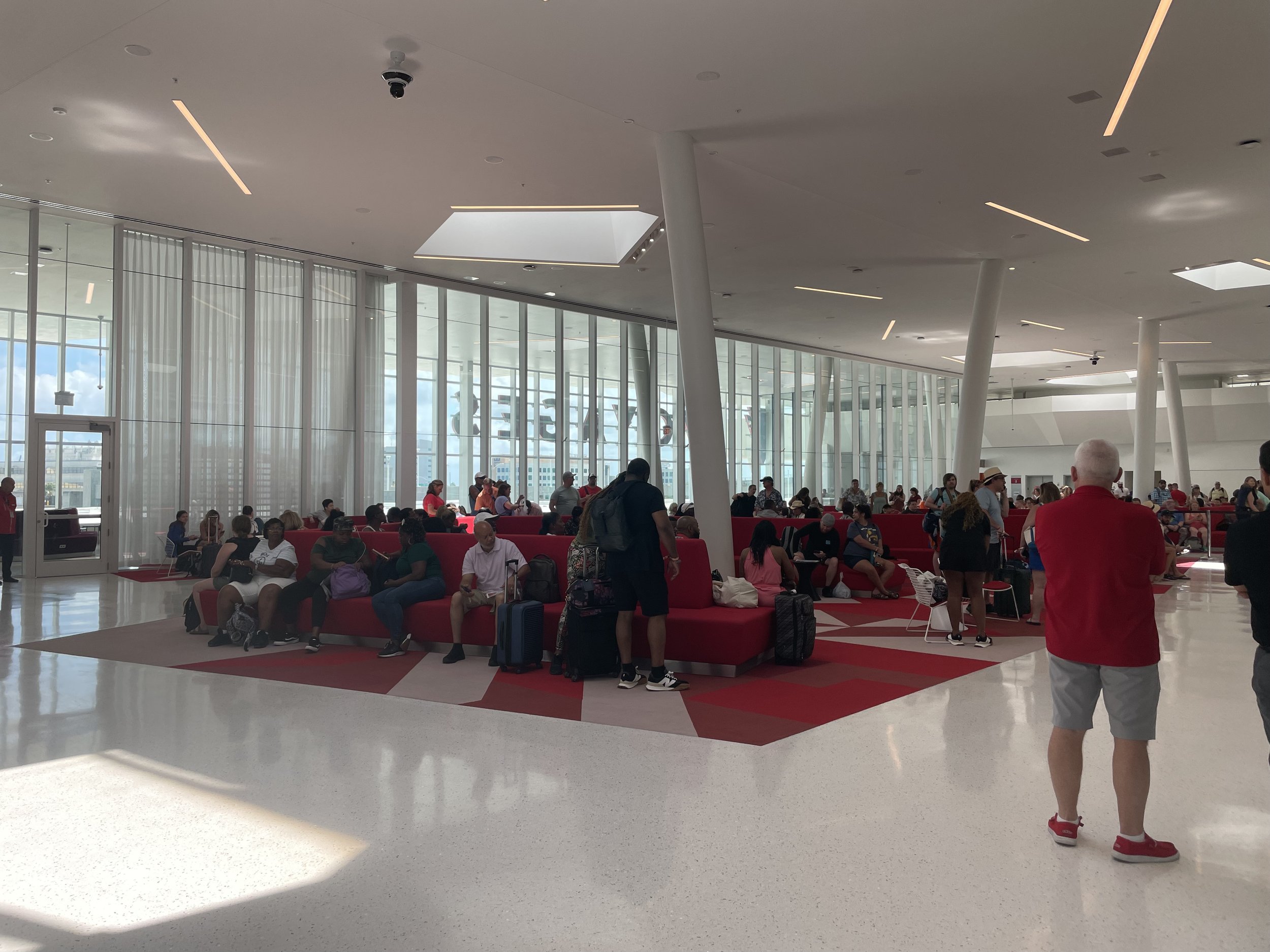Modern cruise ship atrium with red seating and waiting passengers