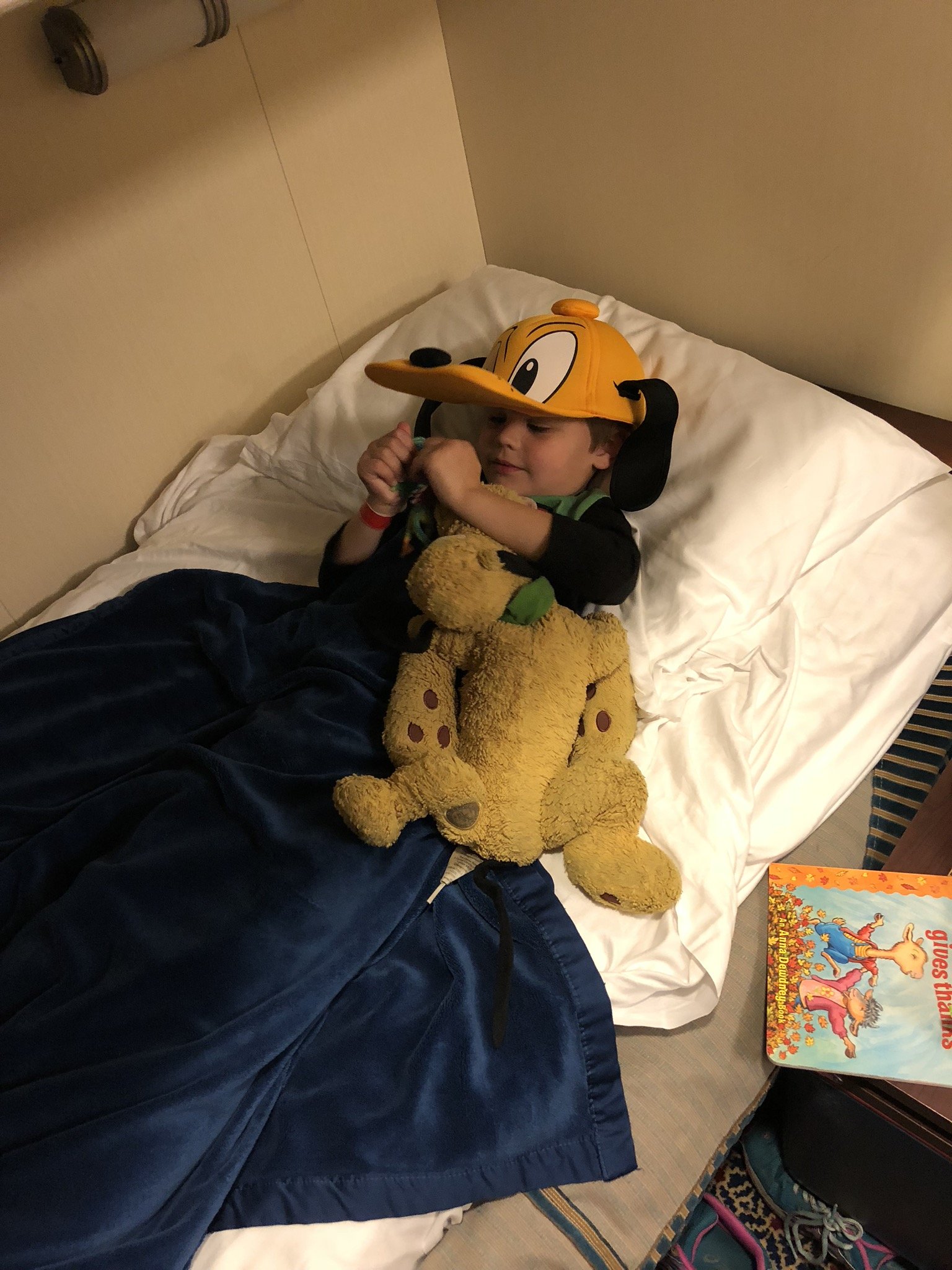Child sleeping with stuffed animal and cartoon character hat in cabin bunk