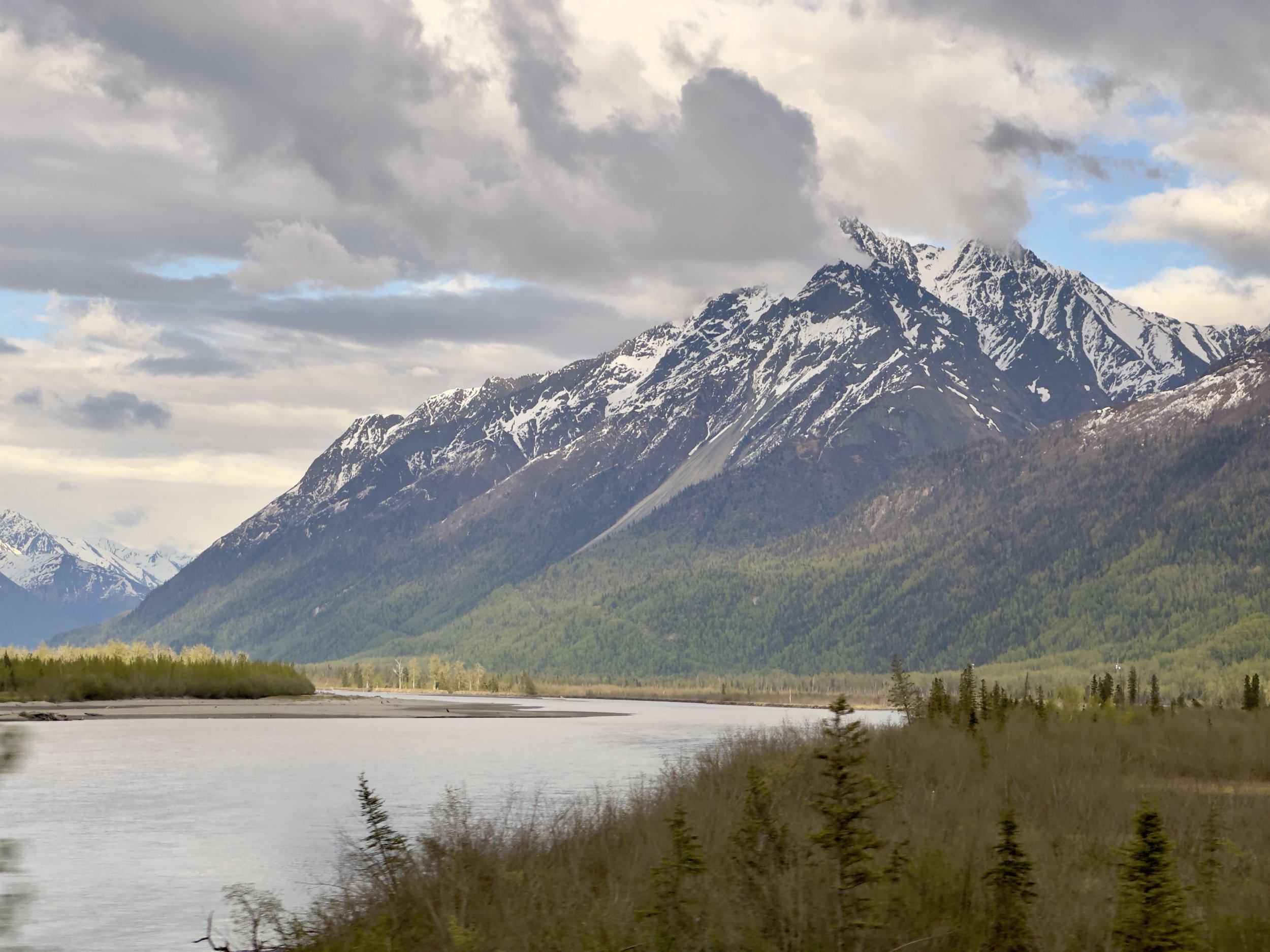 Snow-capped mountain peaks rise above forested valley and river