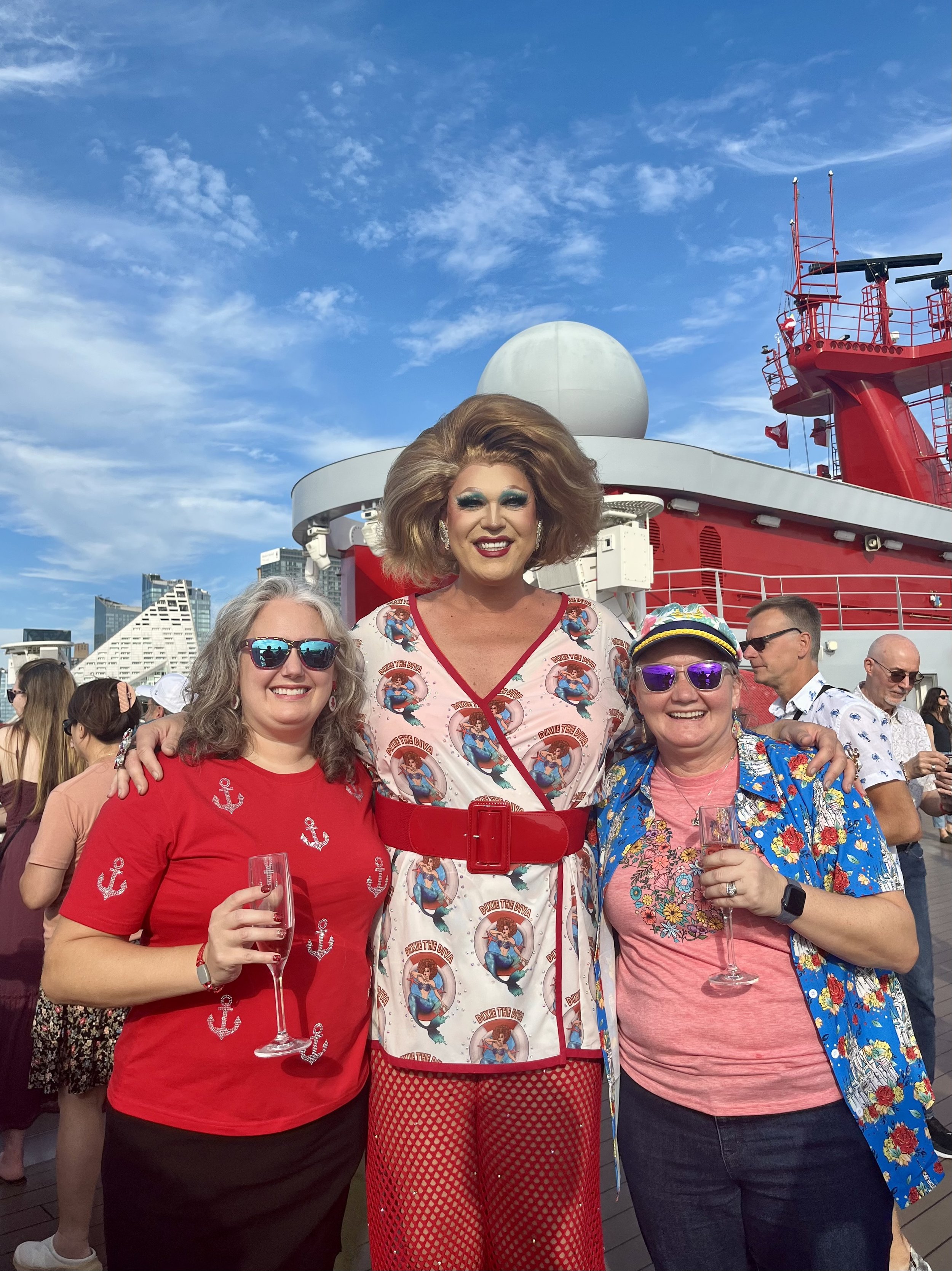 Passengers pose with drag performer on red cruise ship deck