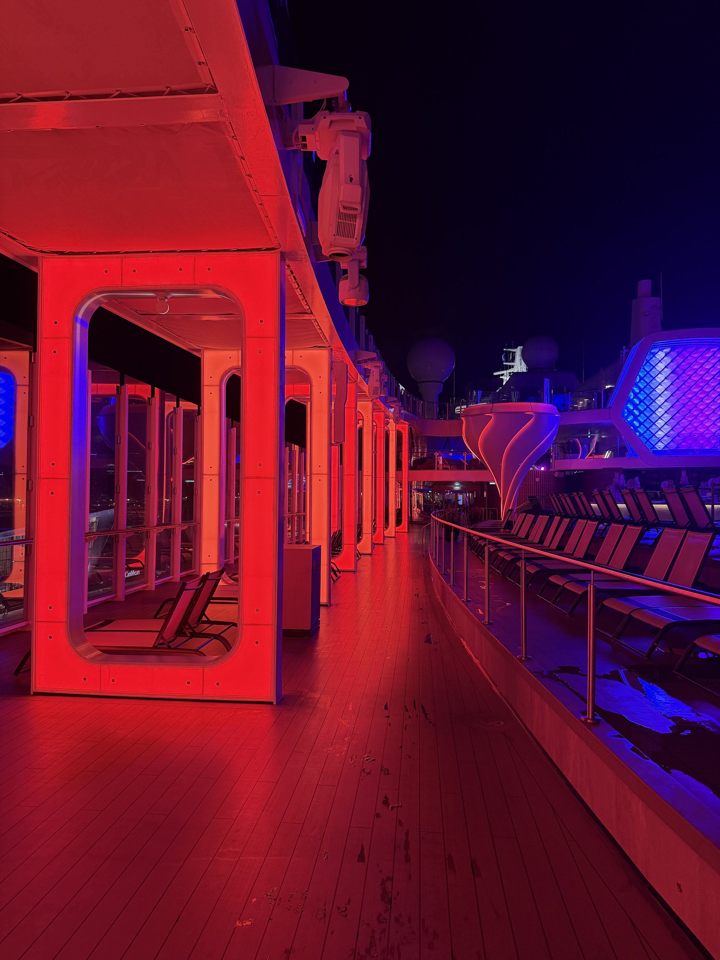 Cruise ship deck at night with red neon lighting and cabin pods