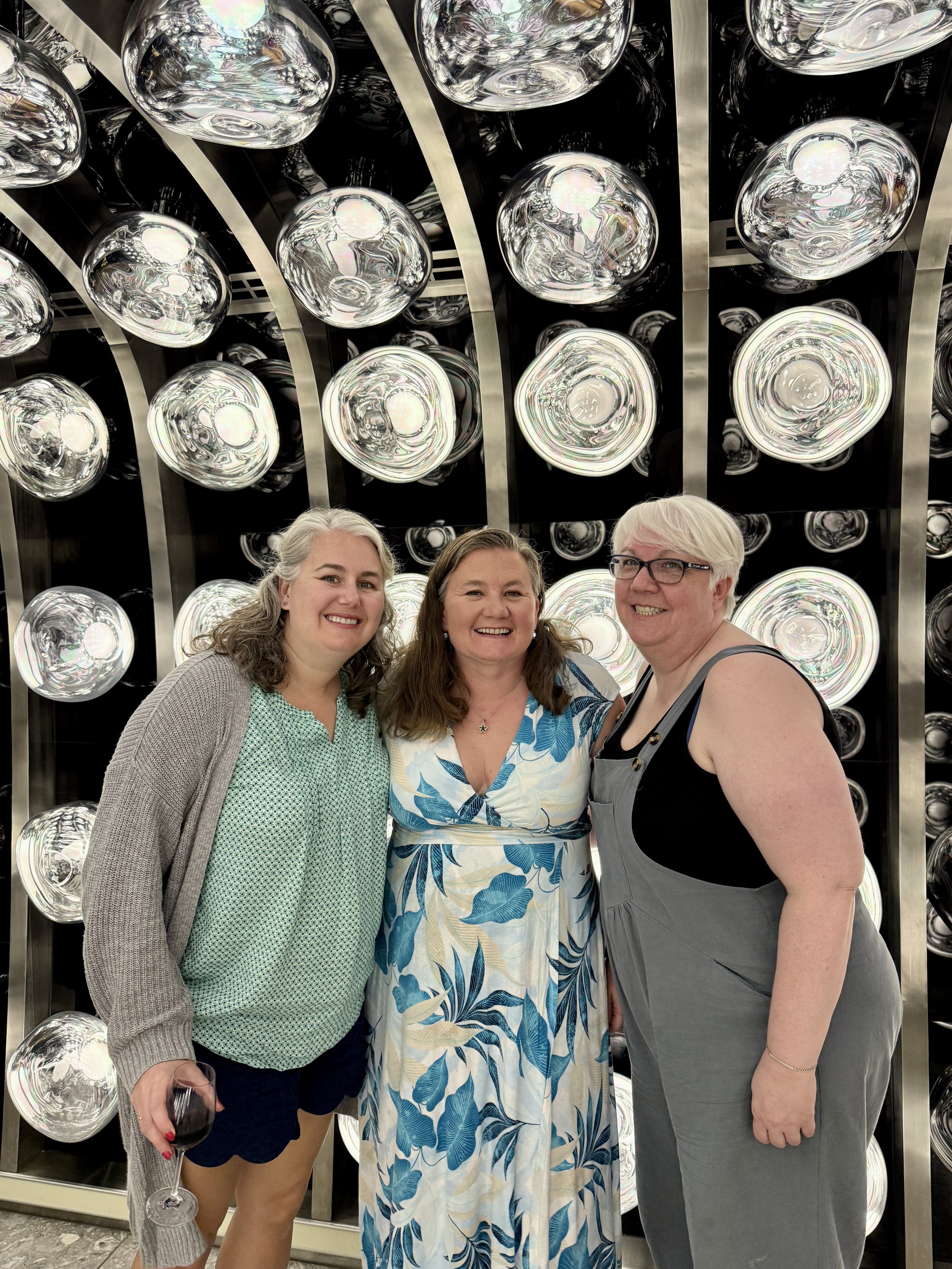Three women posing before illuminated decorative glass bowls