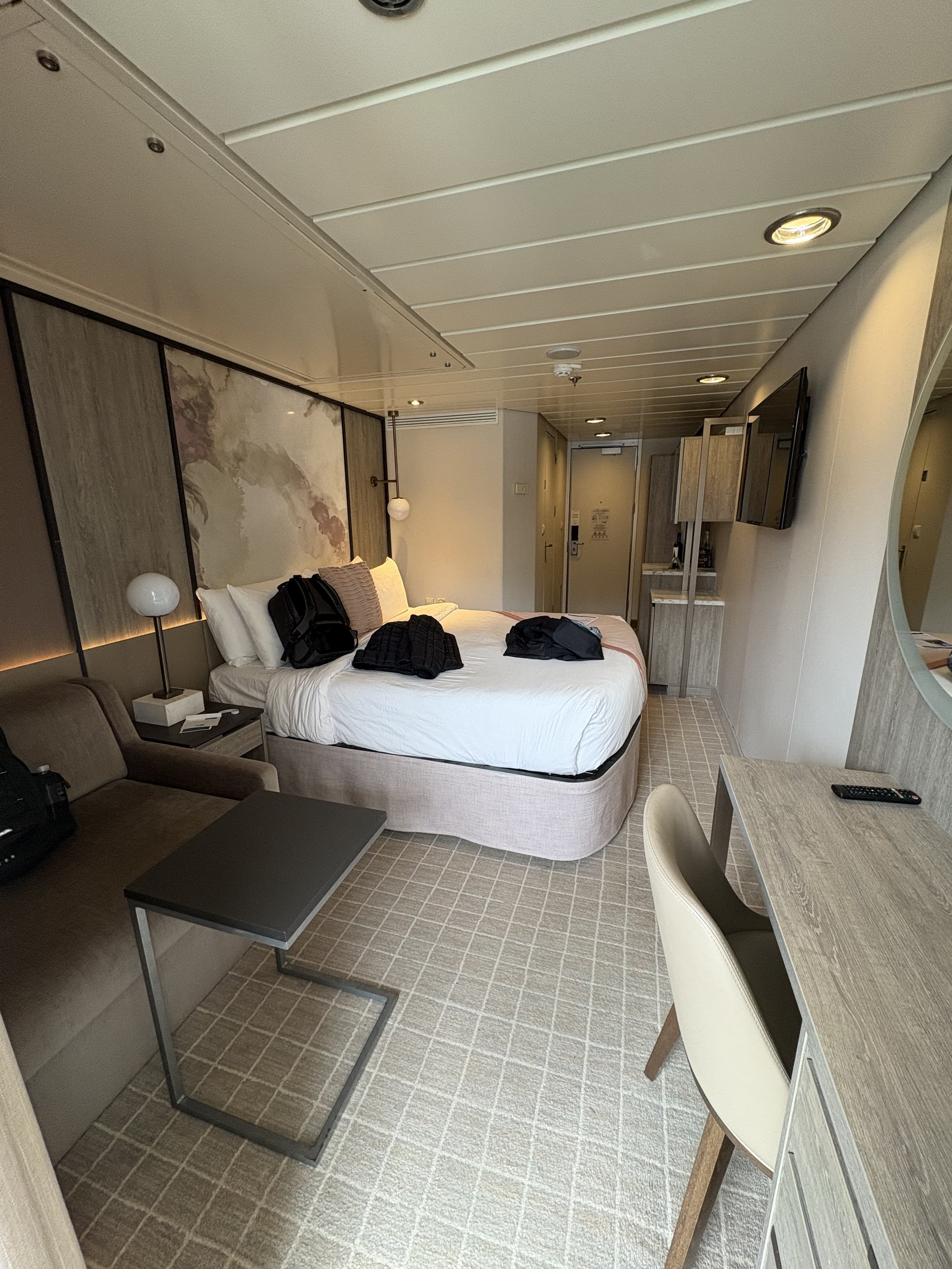 Modern cruise ship stateroom with queen bed and seating area