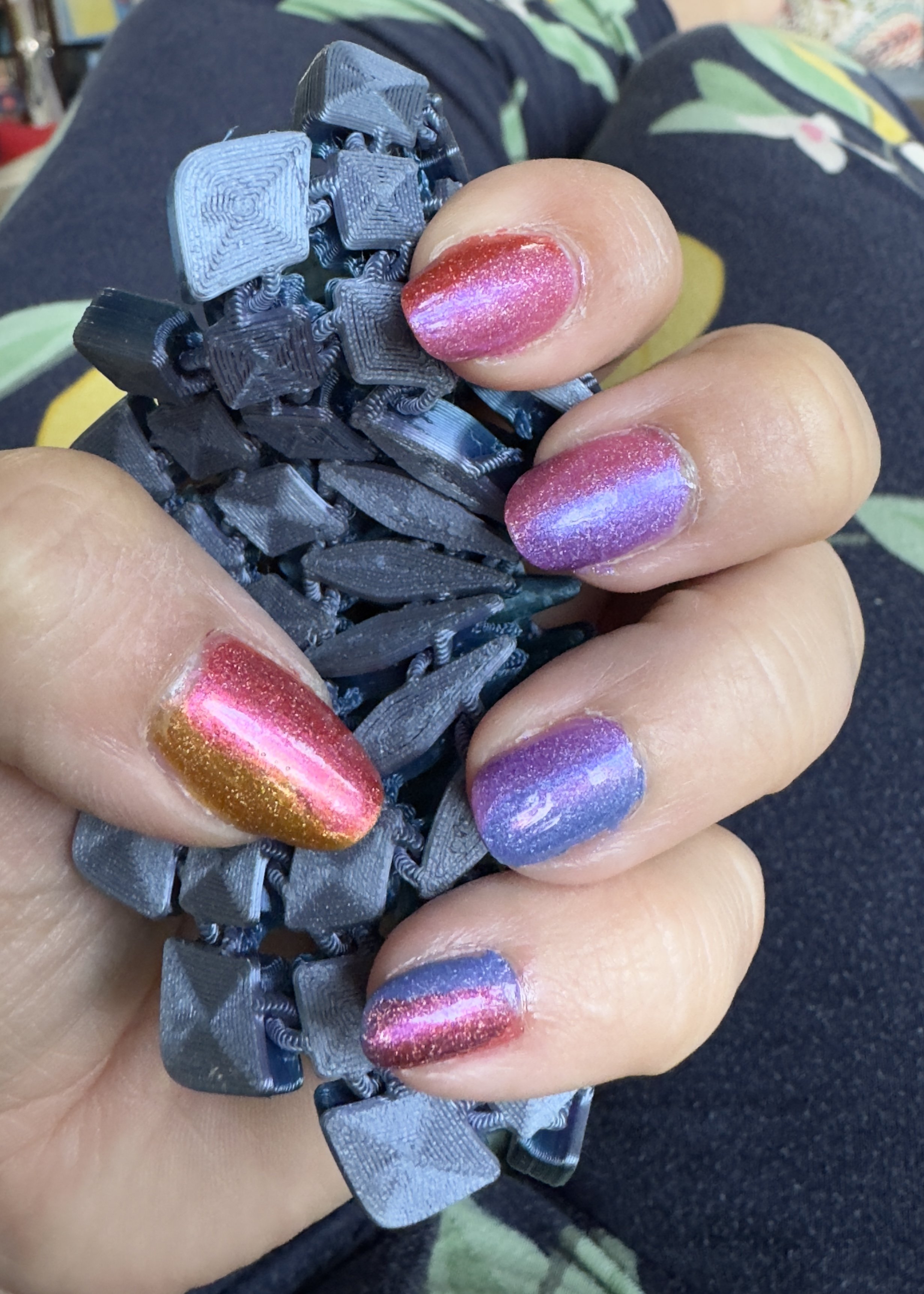 Colorful glitter nail polish manicure displayed on hand holding 3D printed object