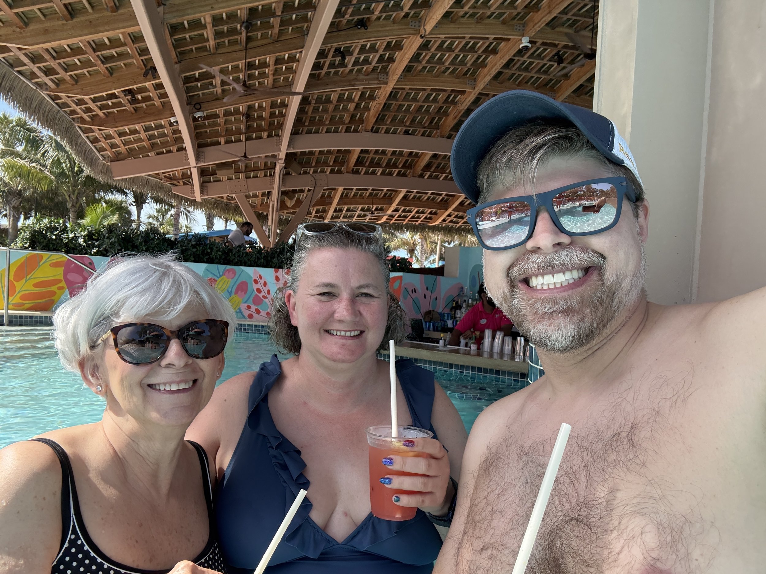 Three people smiling at poolside bar with tropical drinks