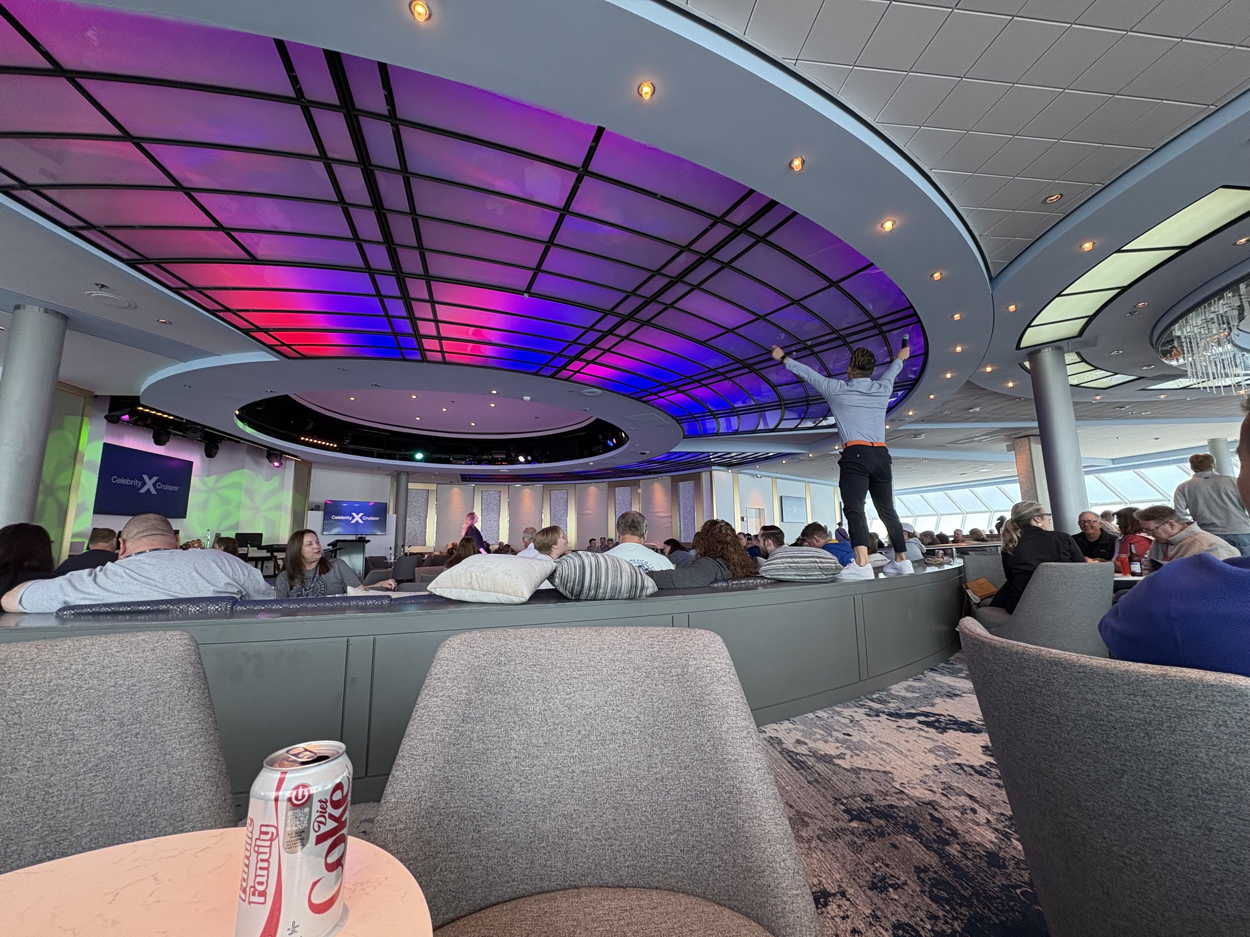 Modern cruise ship lounge with purple neon ceiling and passengers