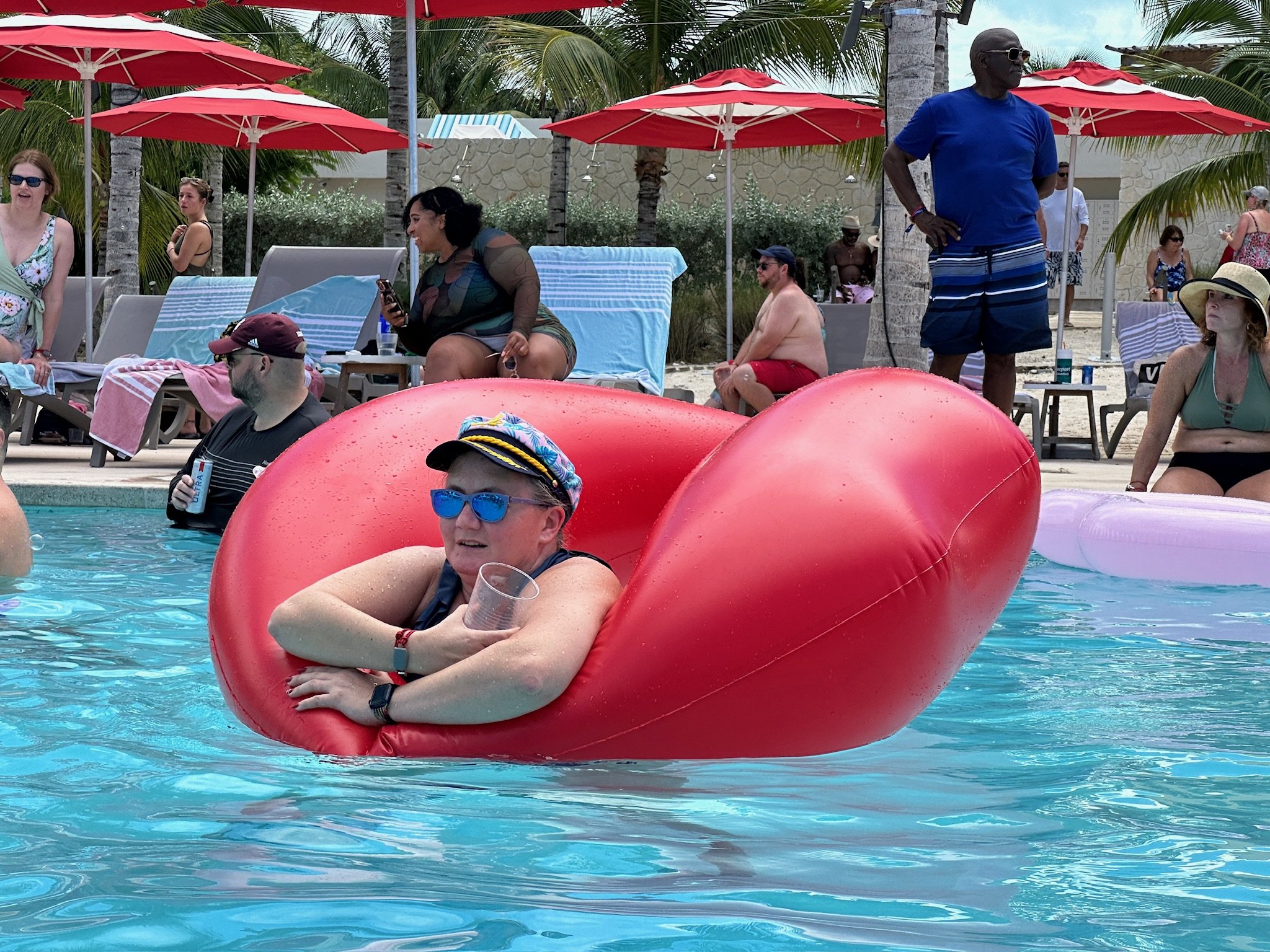 Person floating on giant pink inflatable in tropical pool setting