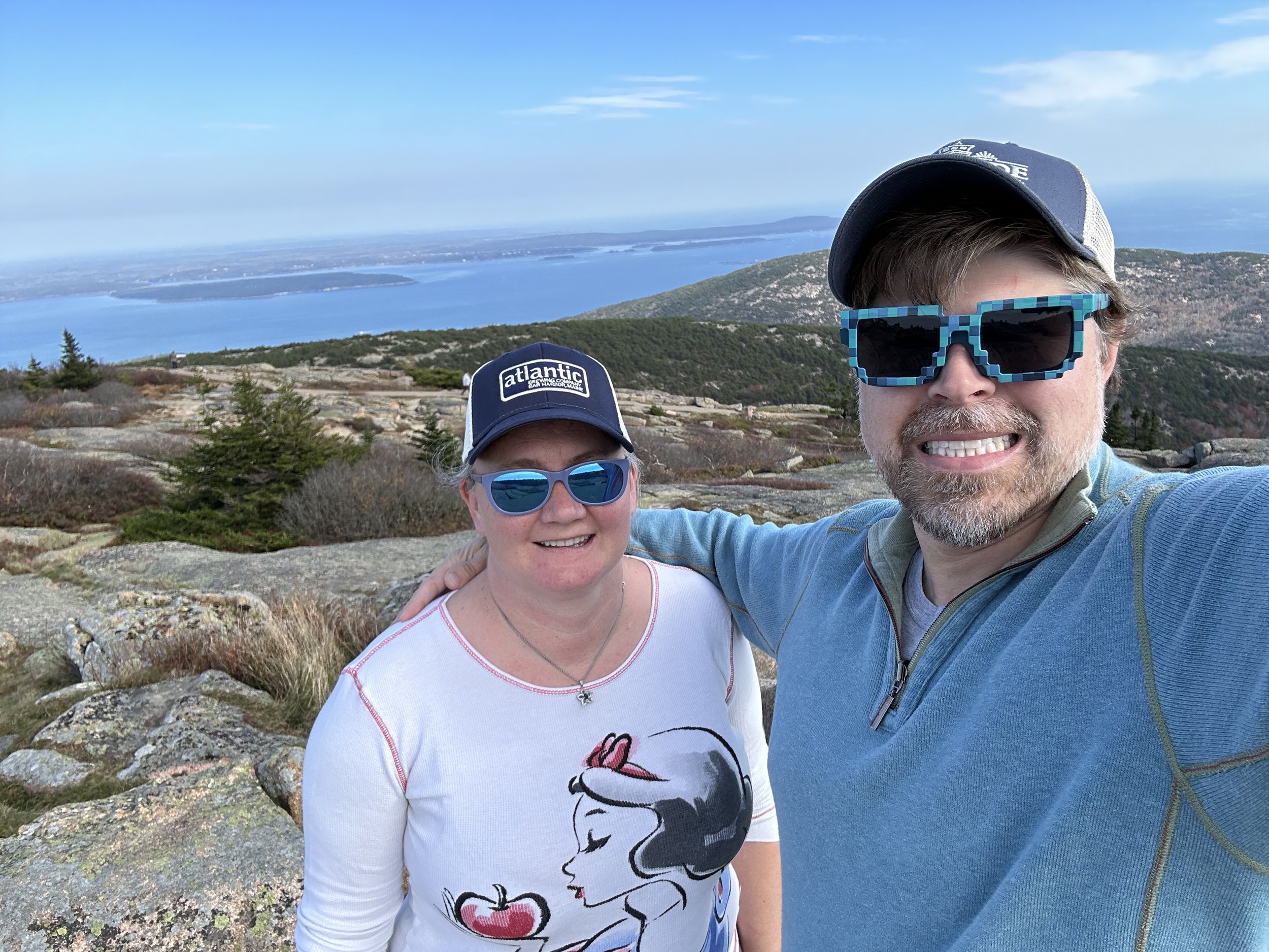 Two smiling tourists at coastal mountain overlook with blue ocean