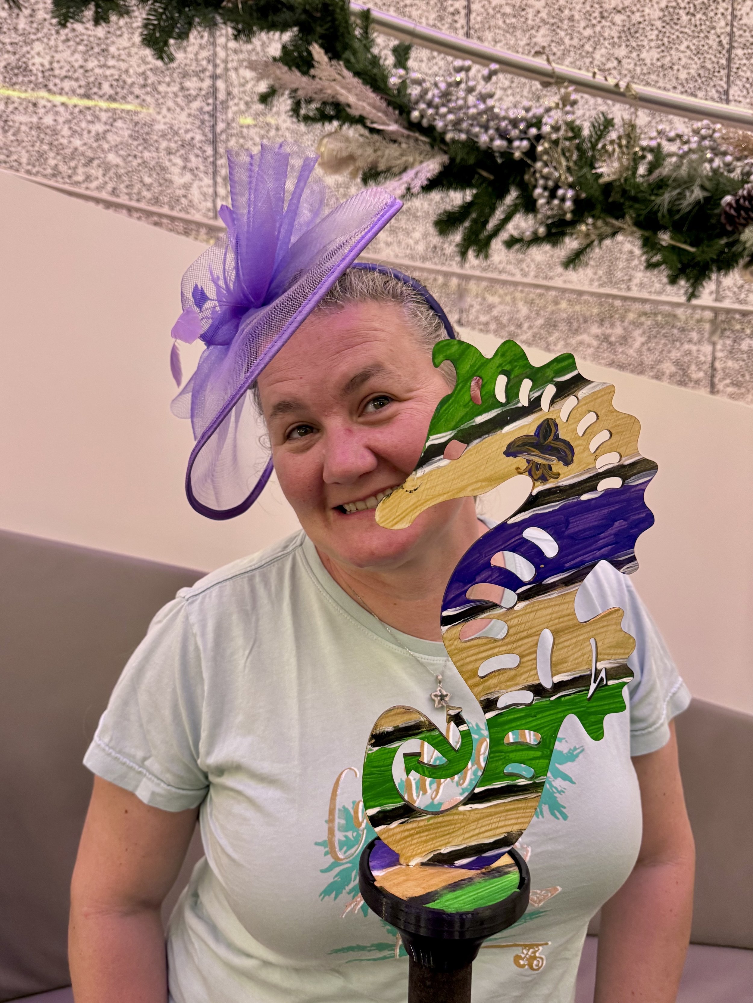 Woman wearing purple fascinator holding colorful wooden ship model