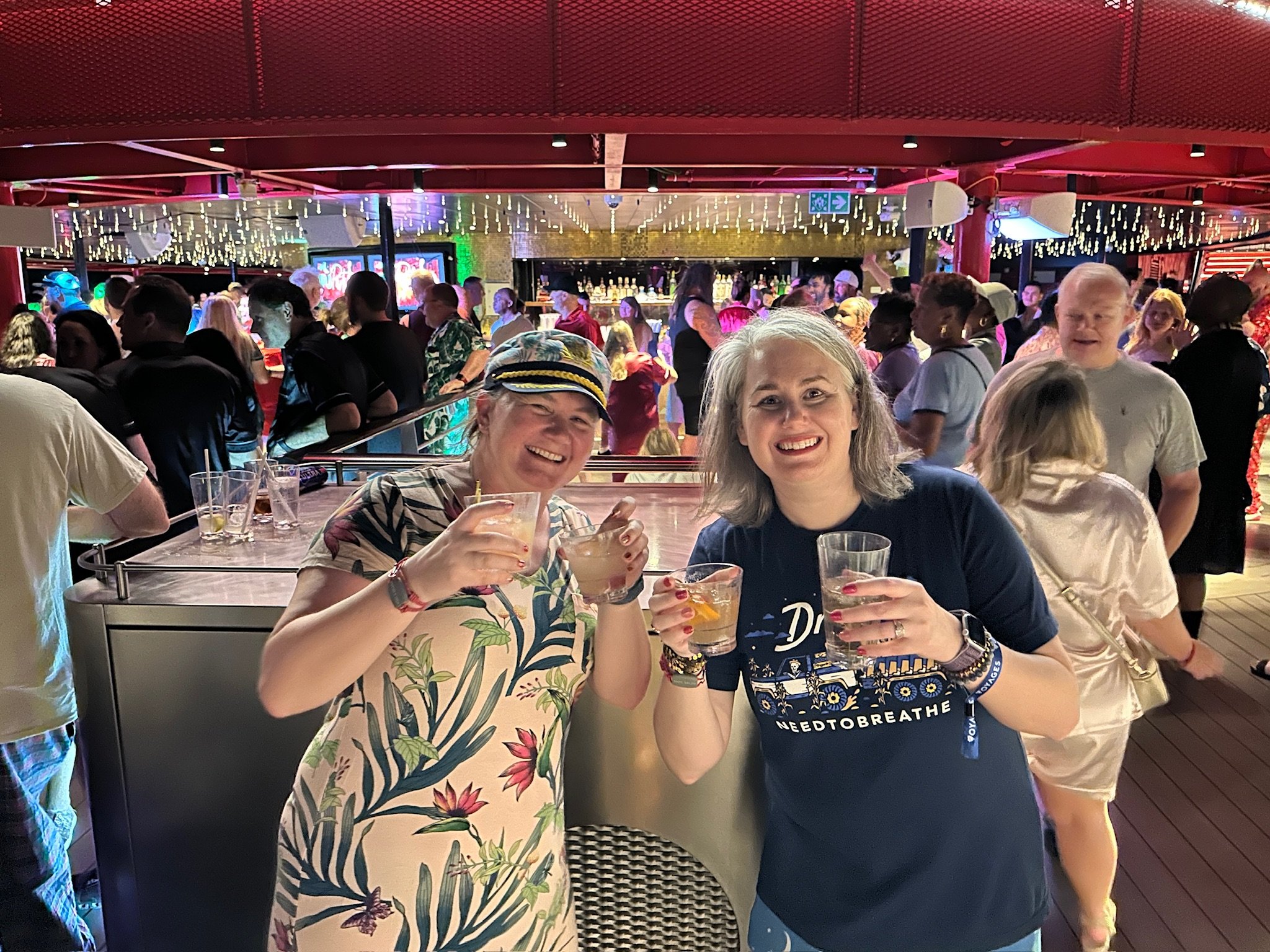 Two women cheers drinks at lively cruise ship bar