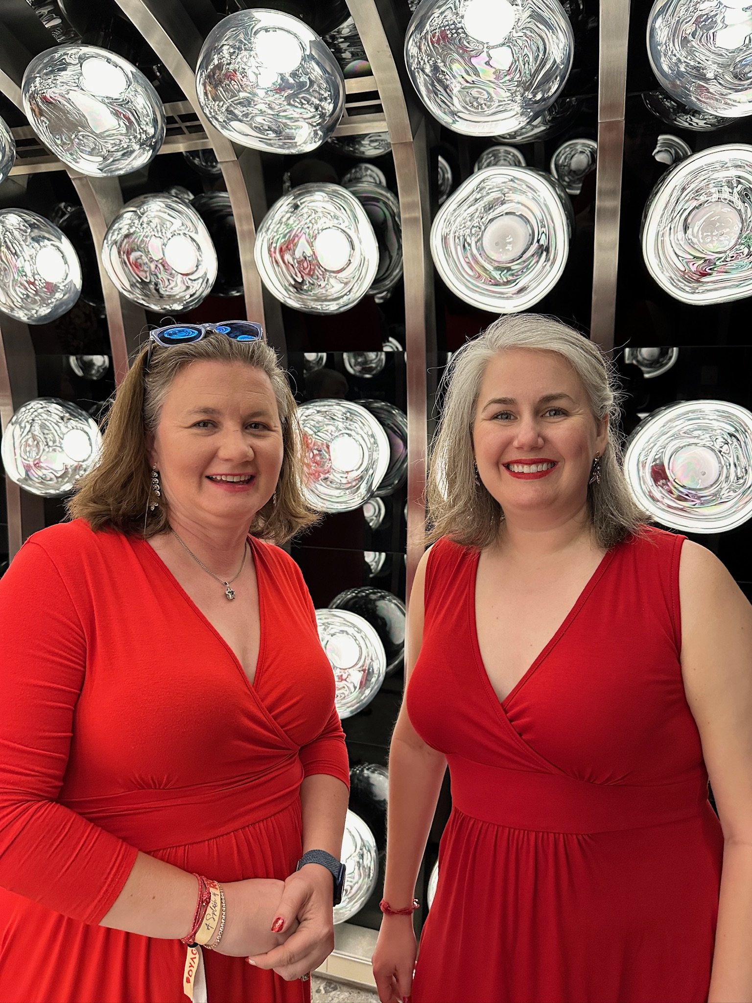 Two women in red dresses pose before stage lights