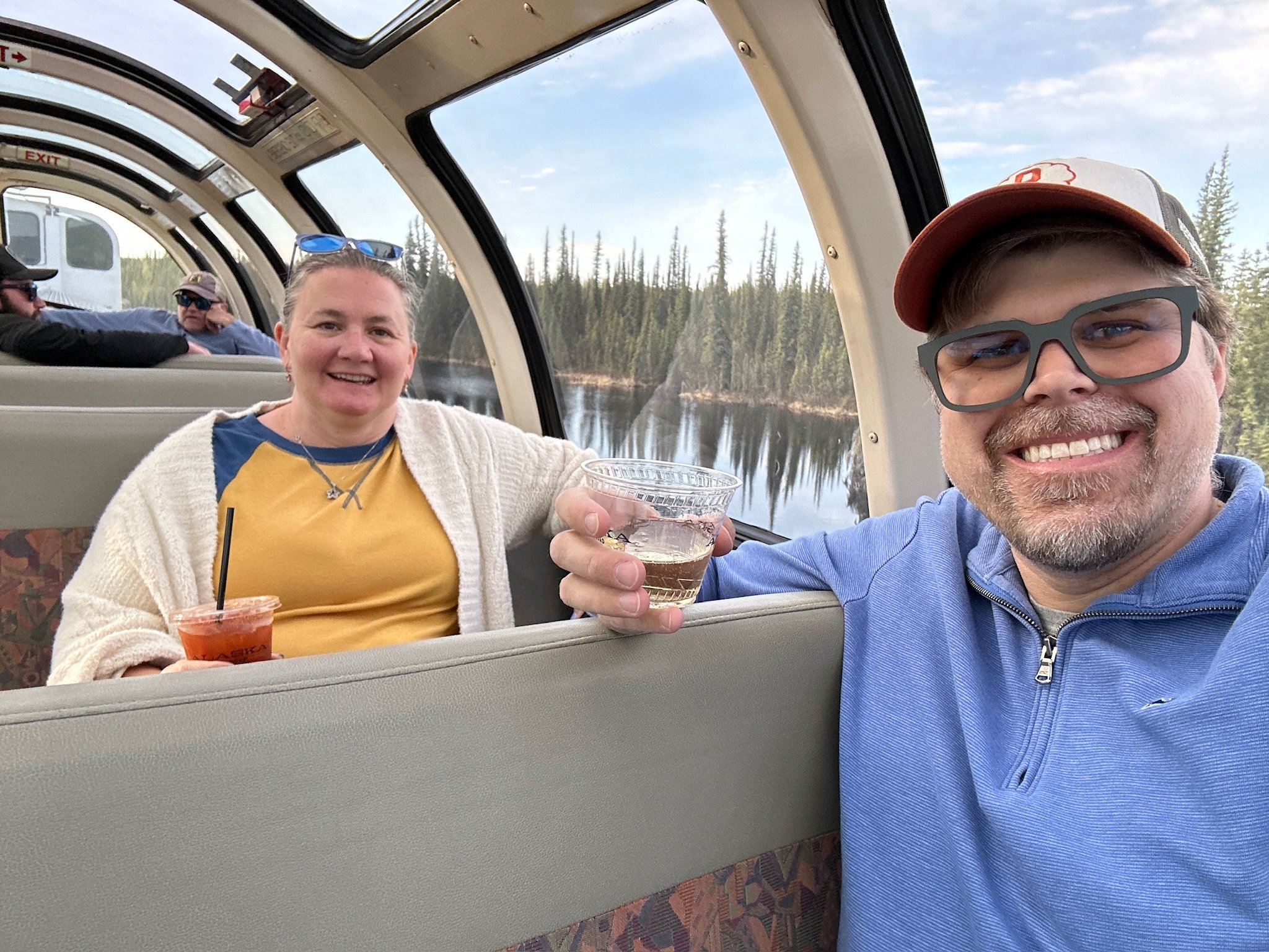 Two passengers enjoying drinks inside seaplane cabin over forested lake