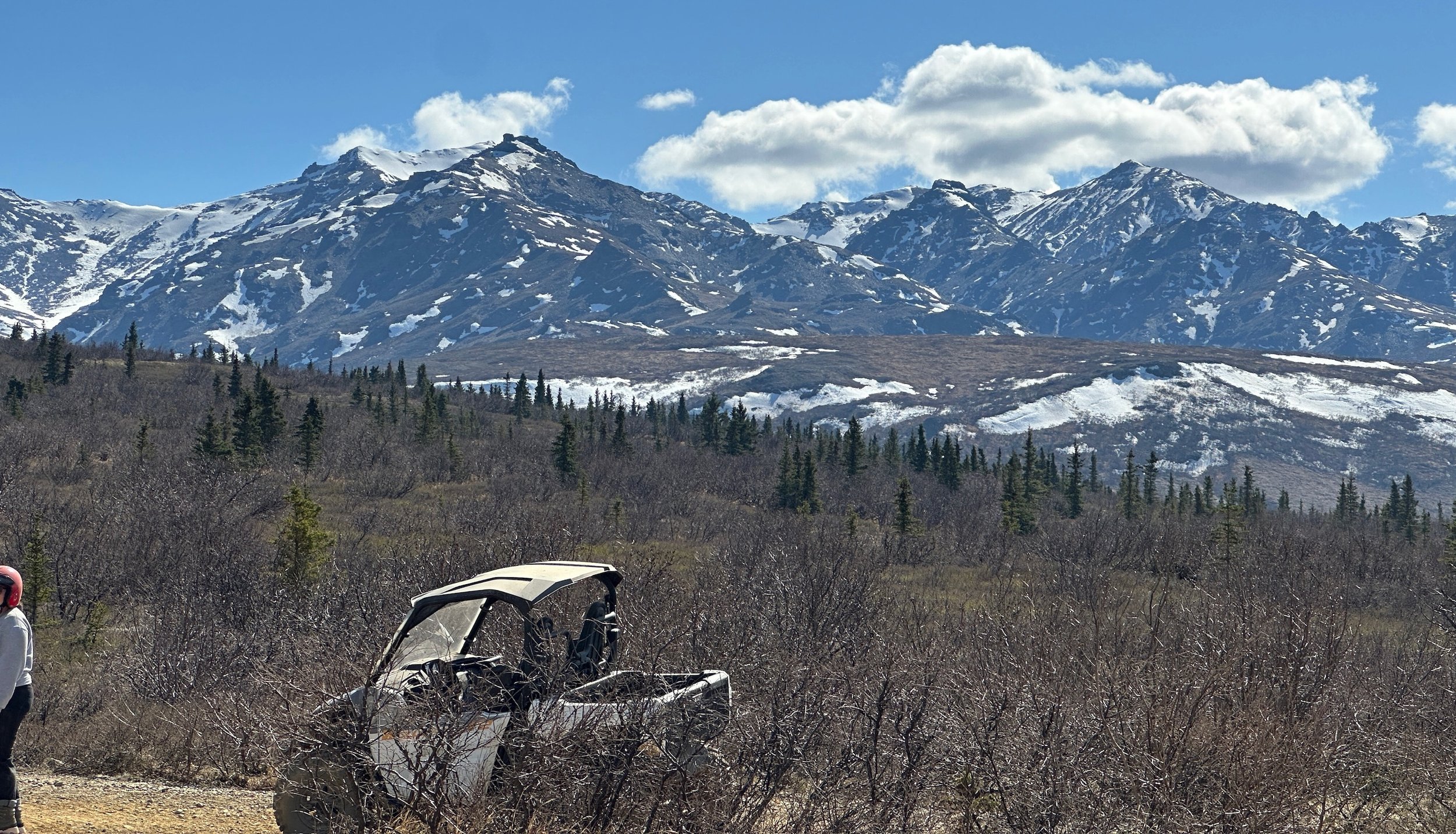 Wrecked vehicle abandoned in Alaskan wilderness with snow-capped mountains