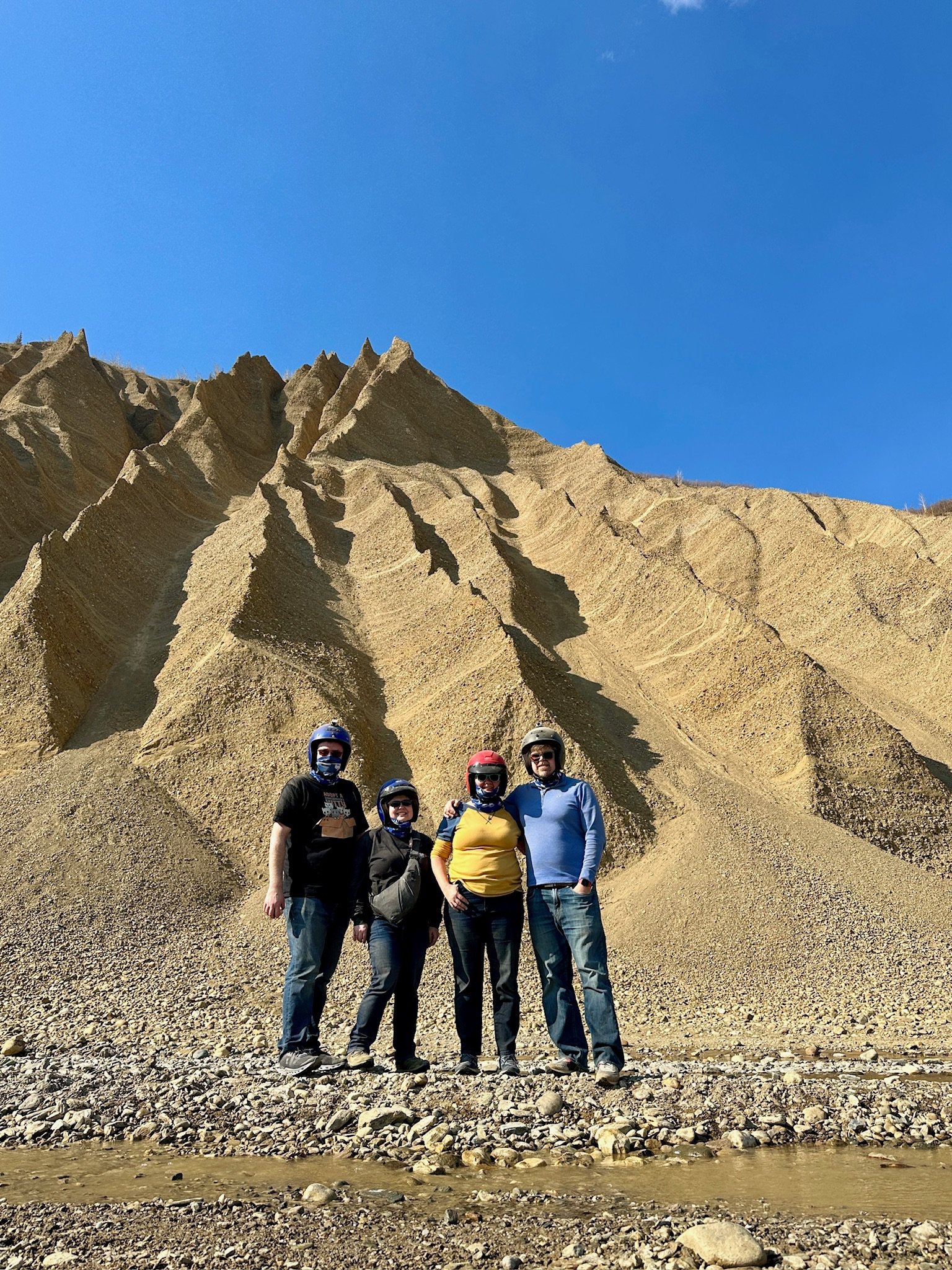 Four people in helmets pose before dramatic badlands terrain