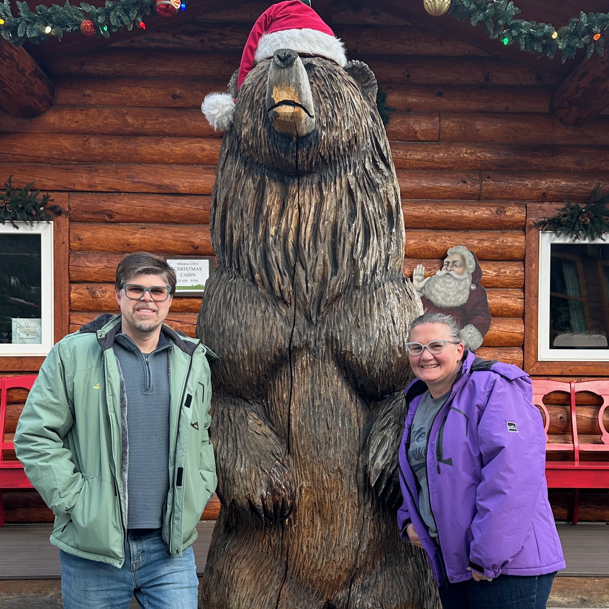 Man and woman pose with carved wooden bear wearing Santa hat