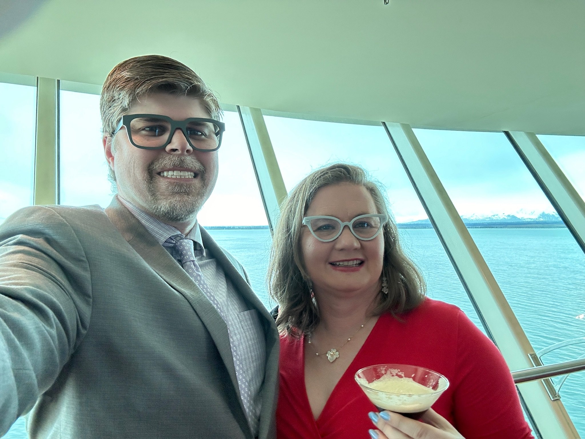 Two people smile on cruise ship deck overlooking ocean