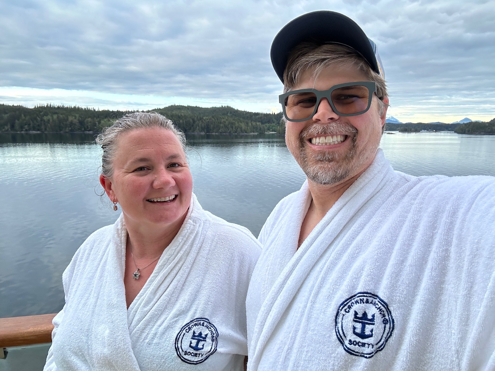 Two guests in spa robes on cruise ship deck overlooking forested lake