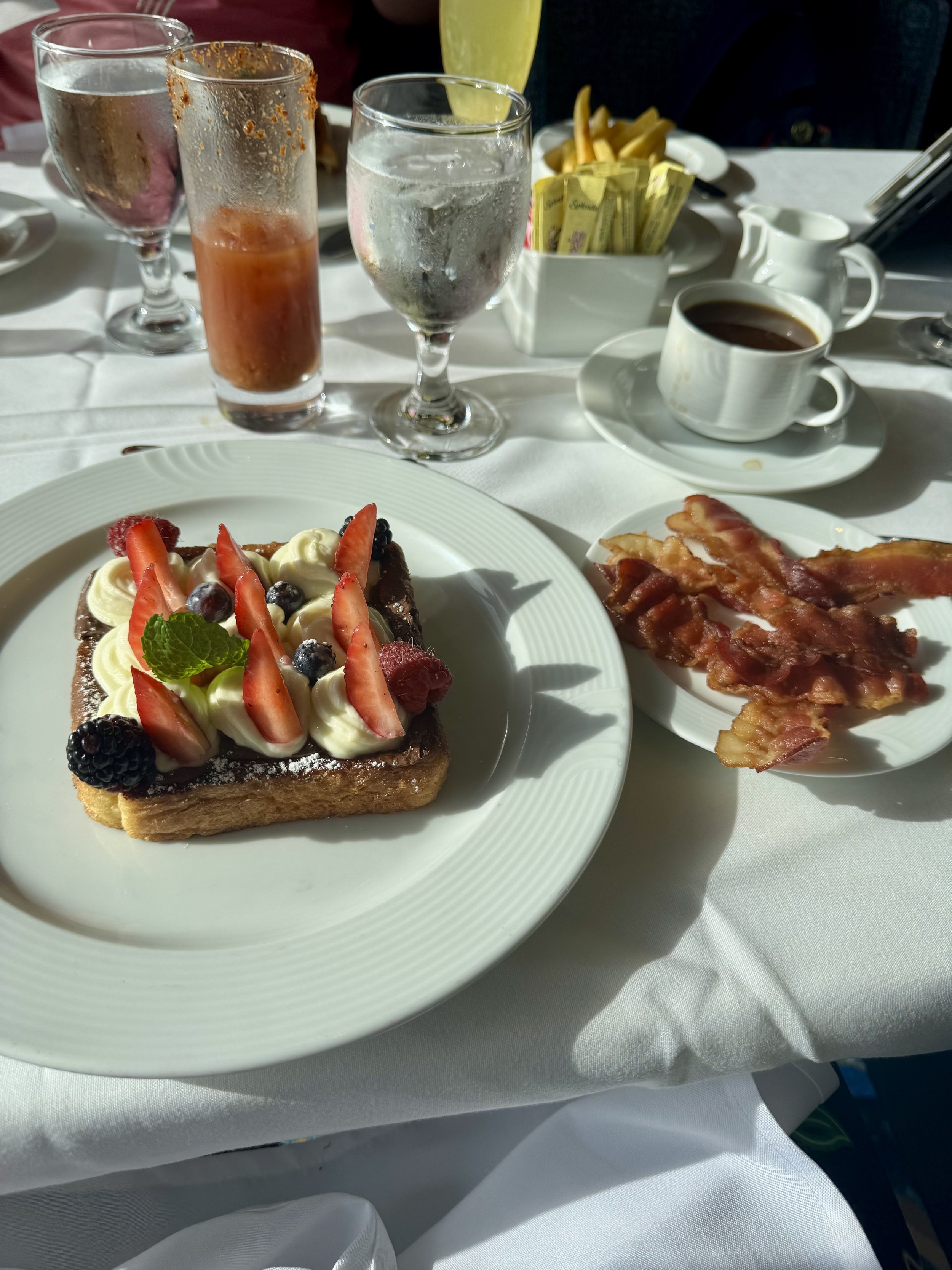 Elegant breakfast platter with fresh berries, pastry, bacon, and beverages