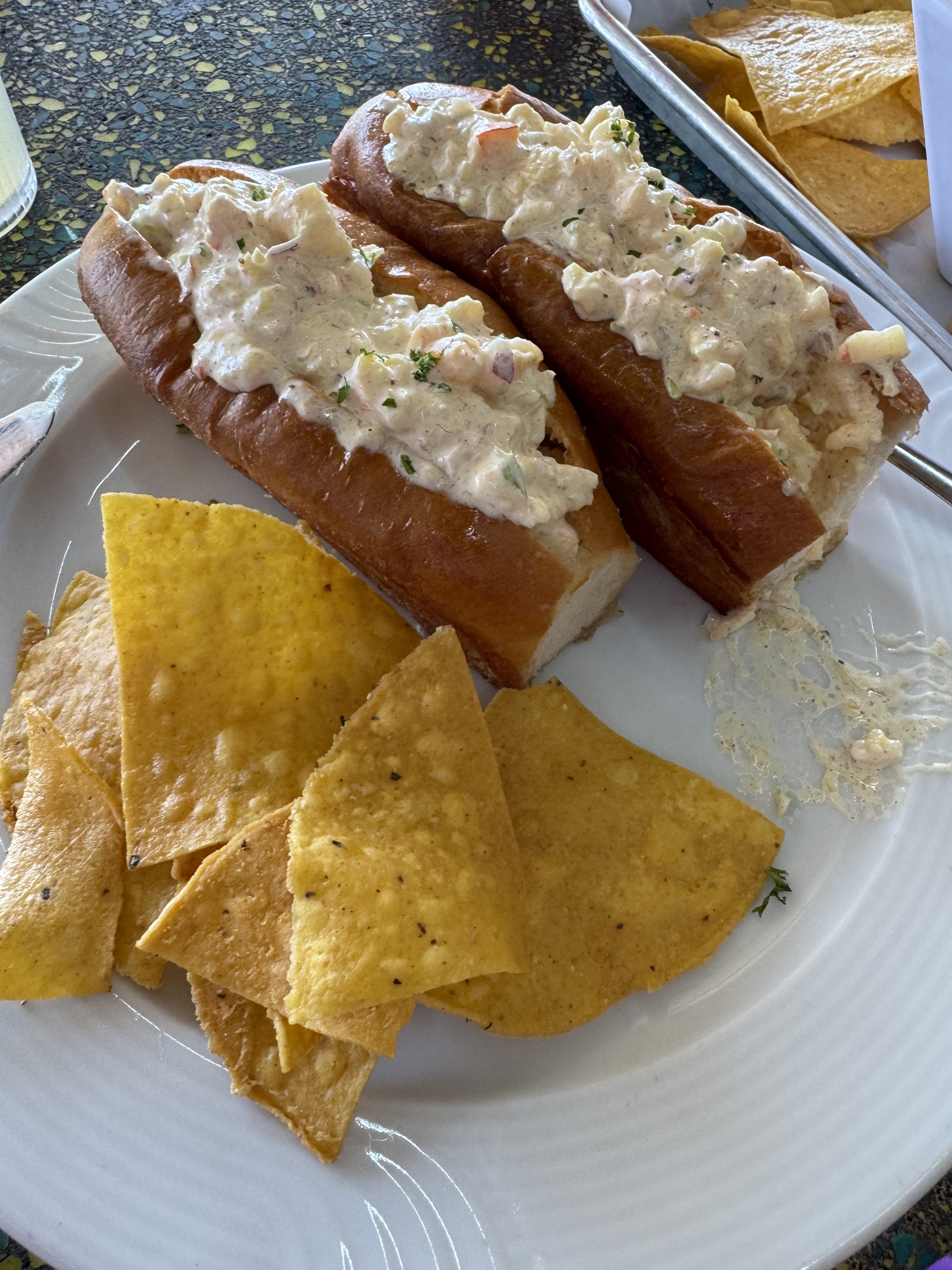 Two lobster rolls with chips on white plate