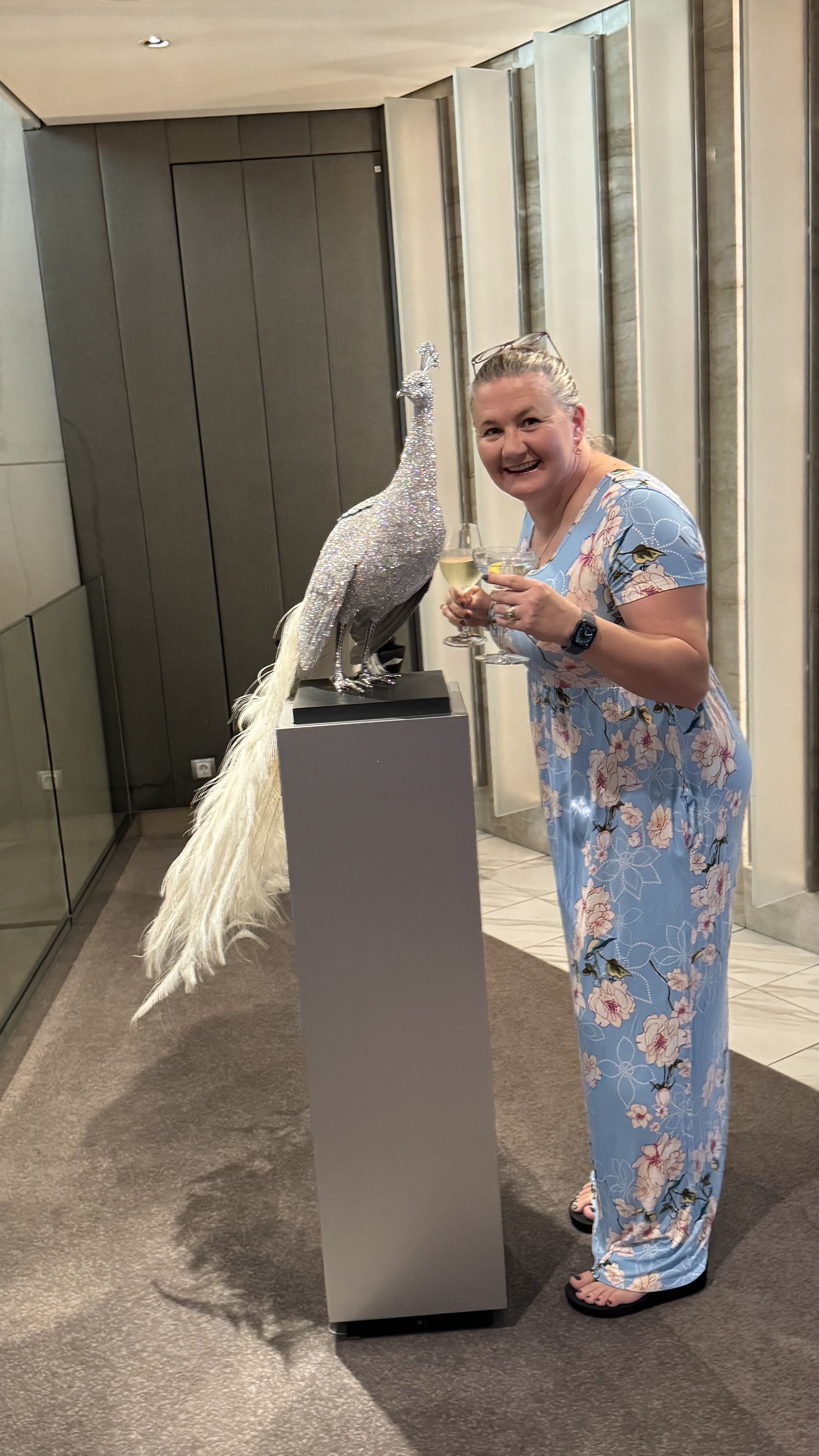 Woman celebrating with champagne next to decorative peacock statue