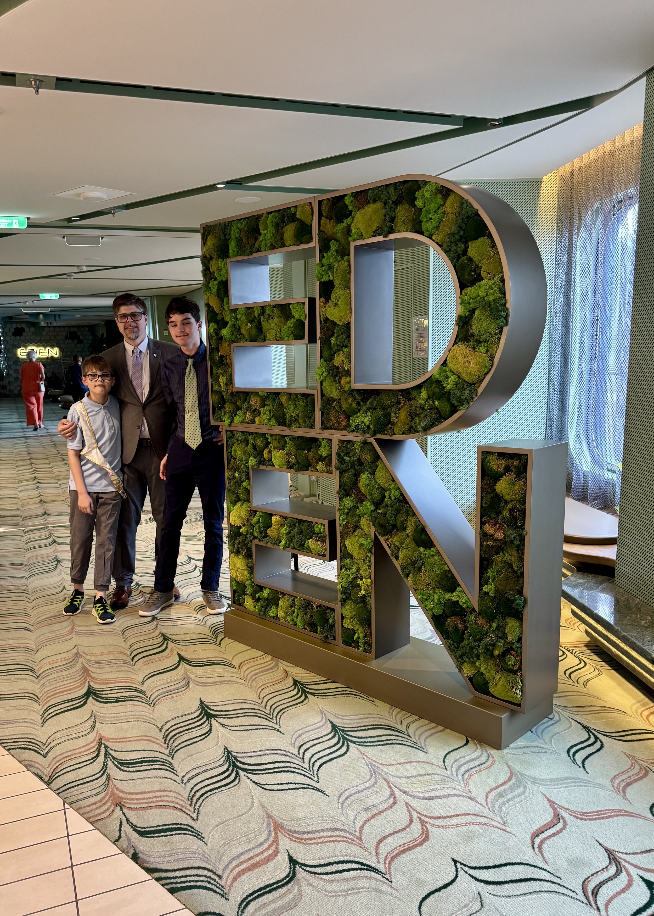 # Three people pose with large letter R moss wall installation