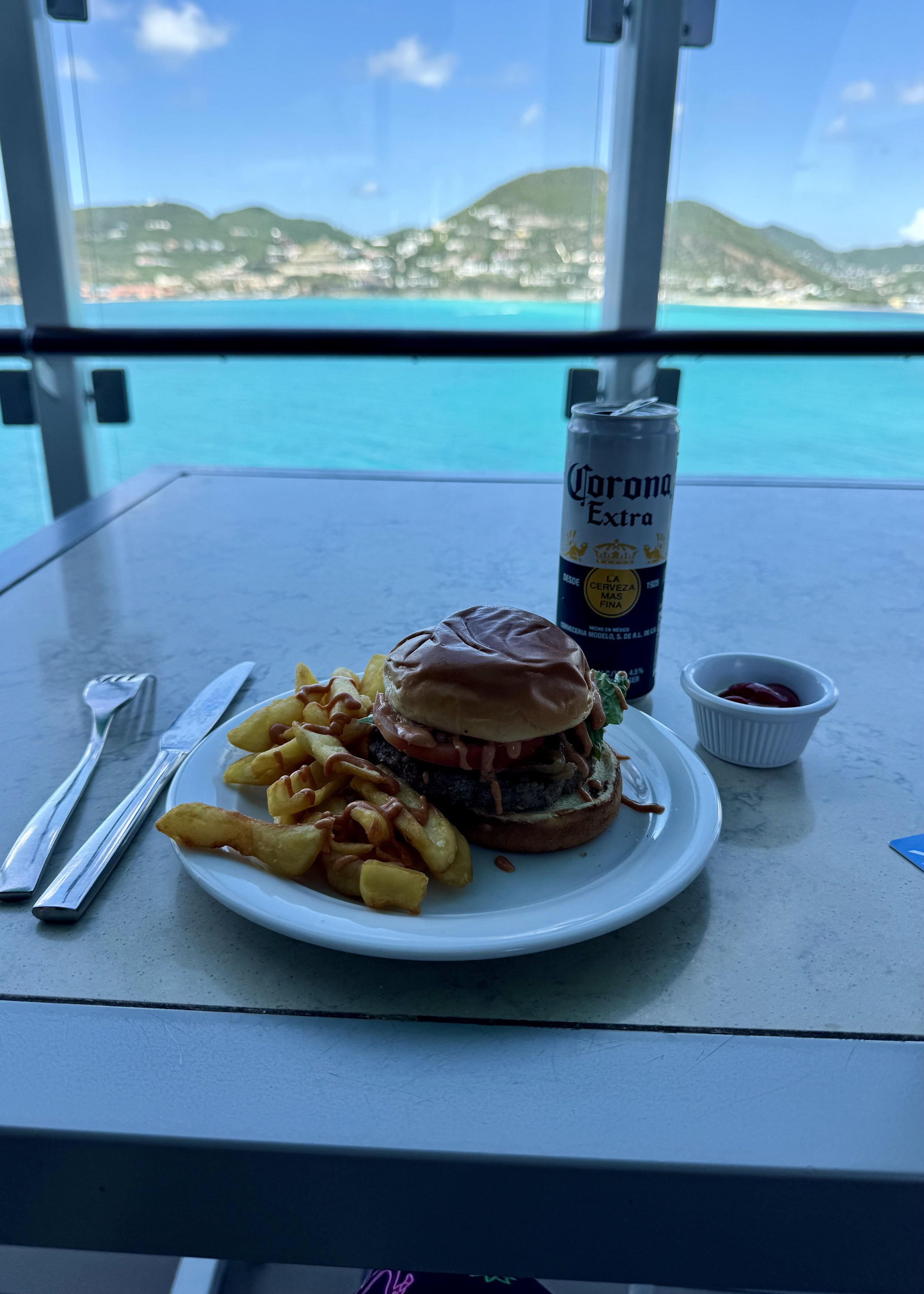 Burger and fries with Corona beer, scenic coastal hills view from ship