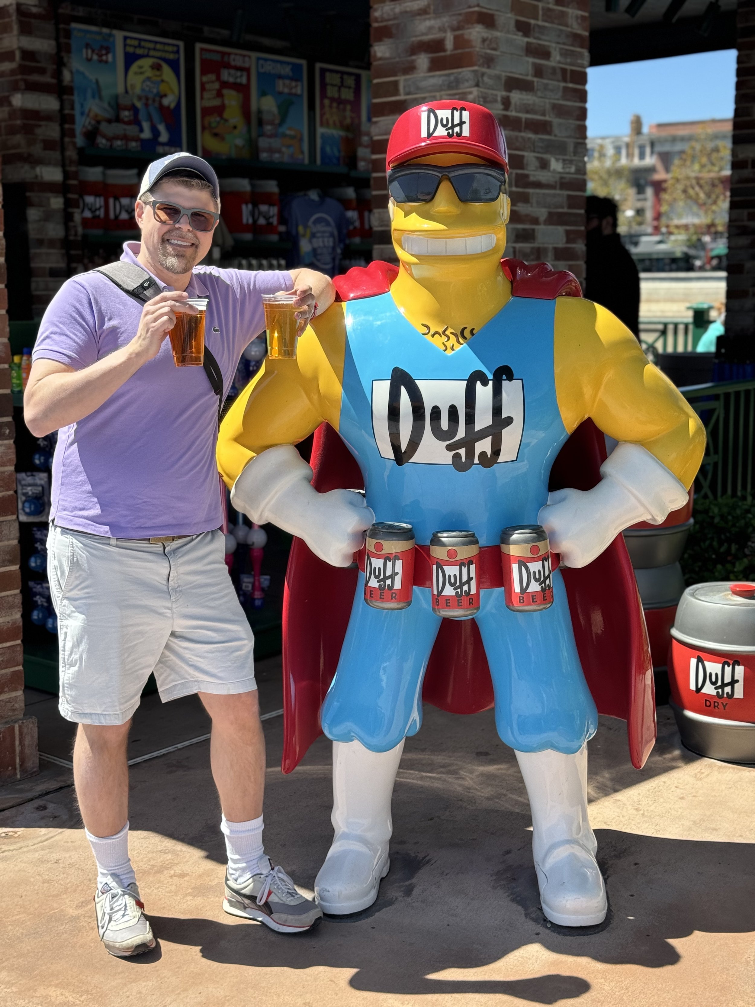 Man poses with Duff Beer mascot holding beers at theme park