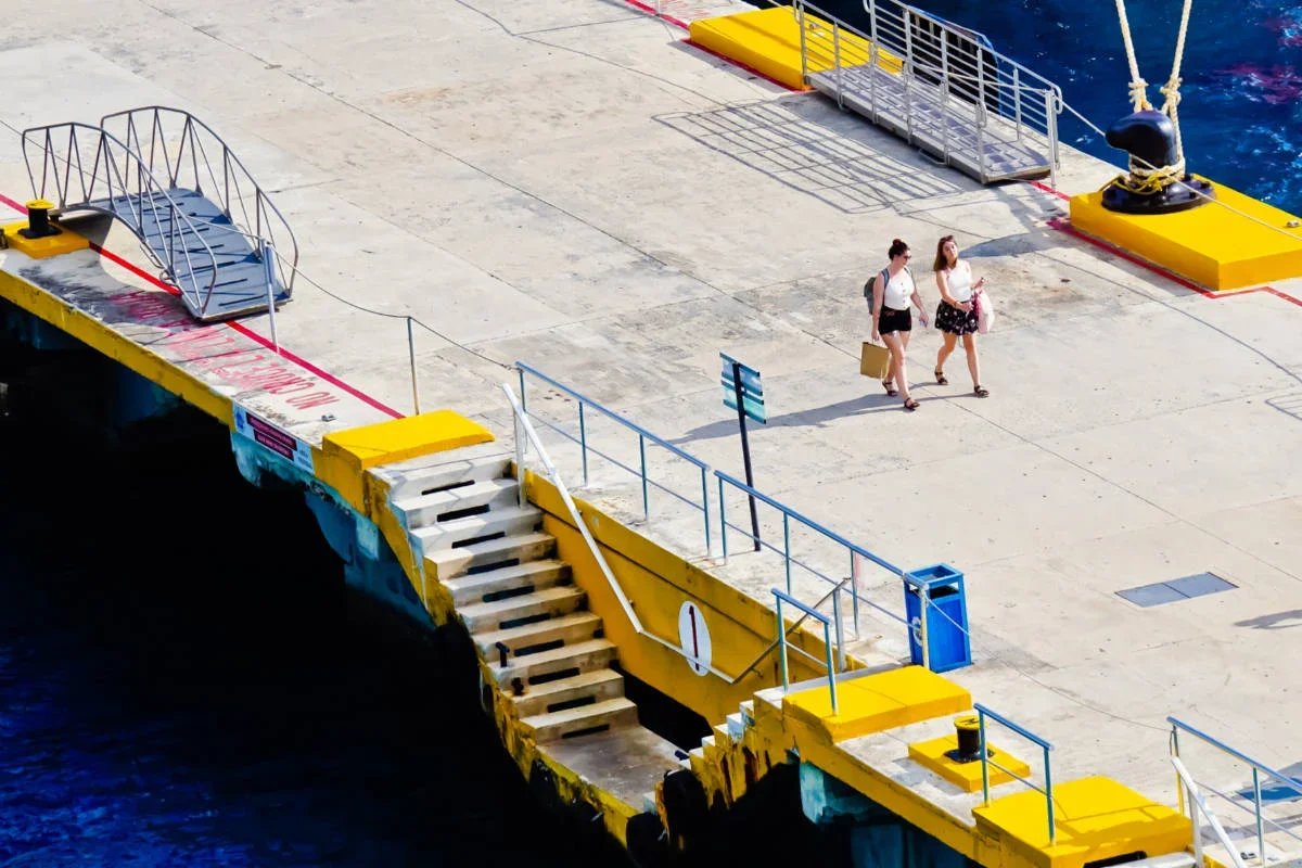 Two passengers walking on yellow and blue cruise ship dock