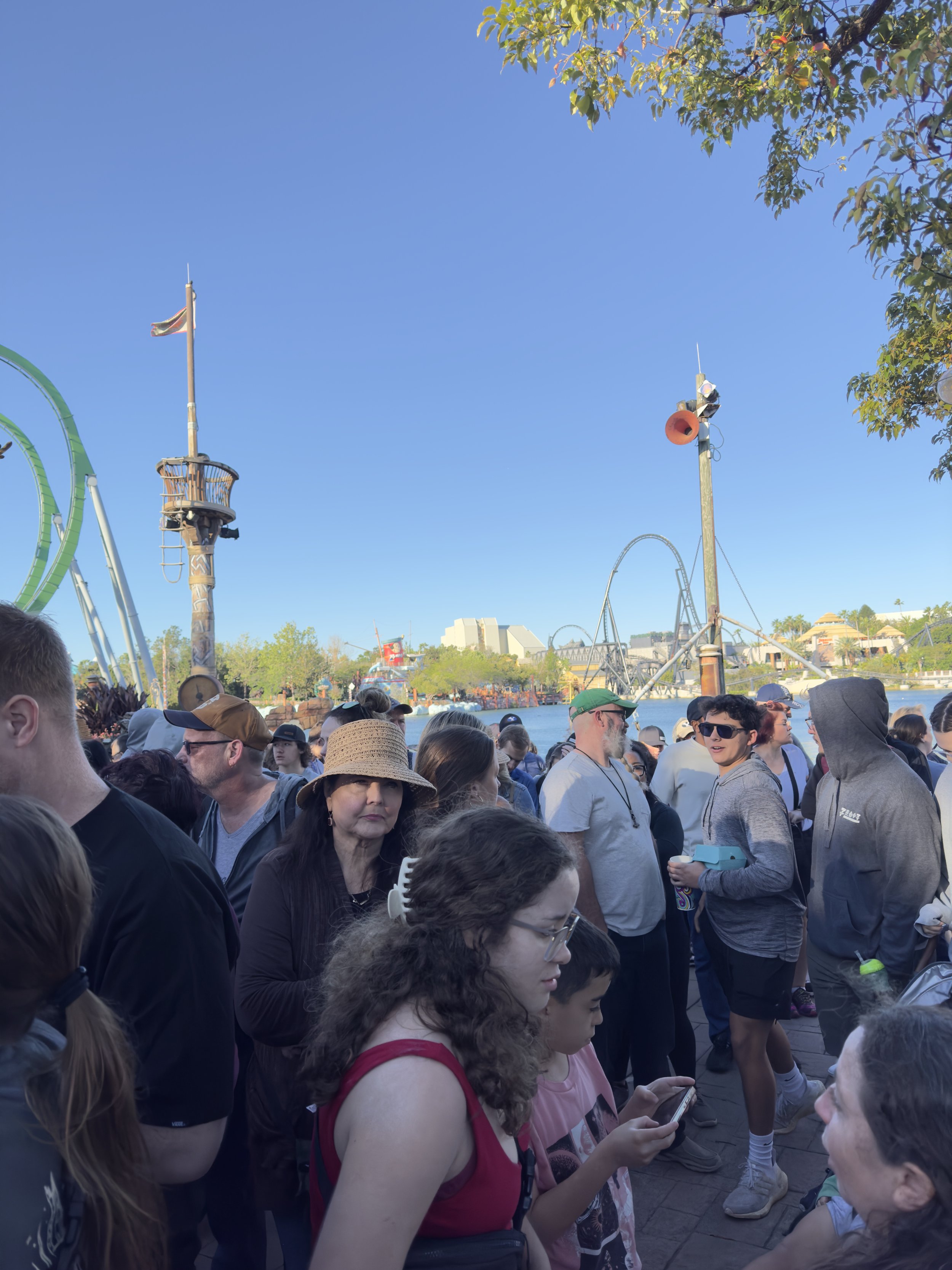 Crowds gather at theme park waterfront with roller coasters and ships