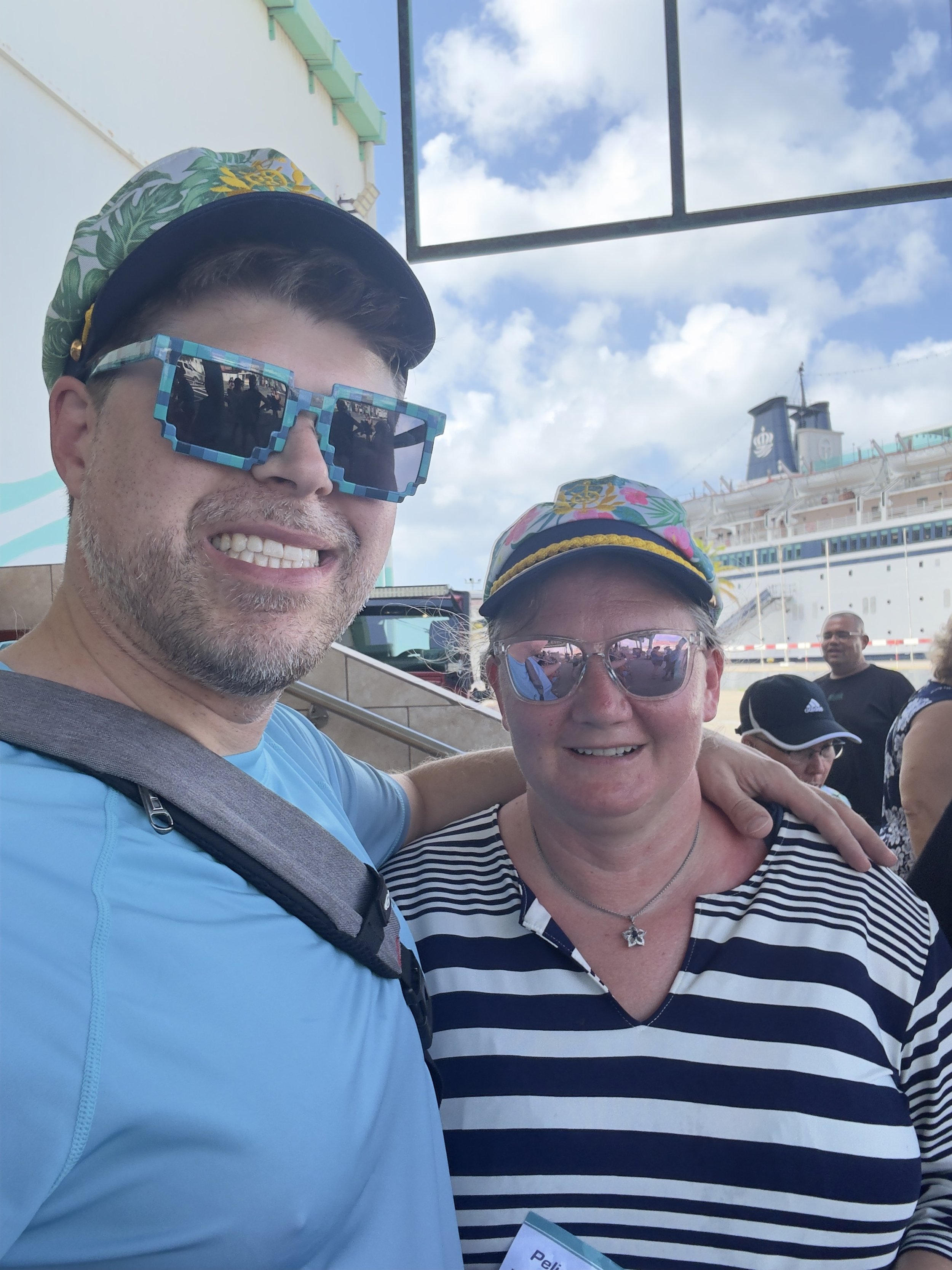 Two friends pose at cruise port with large ship behind them